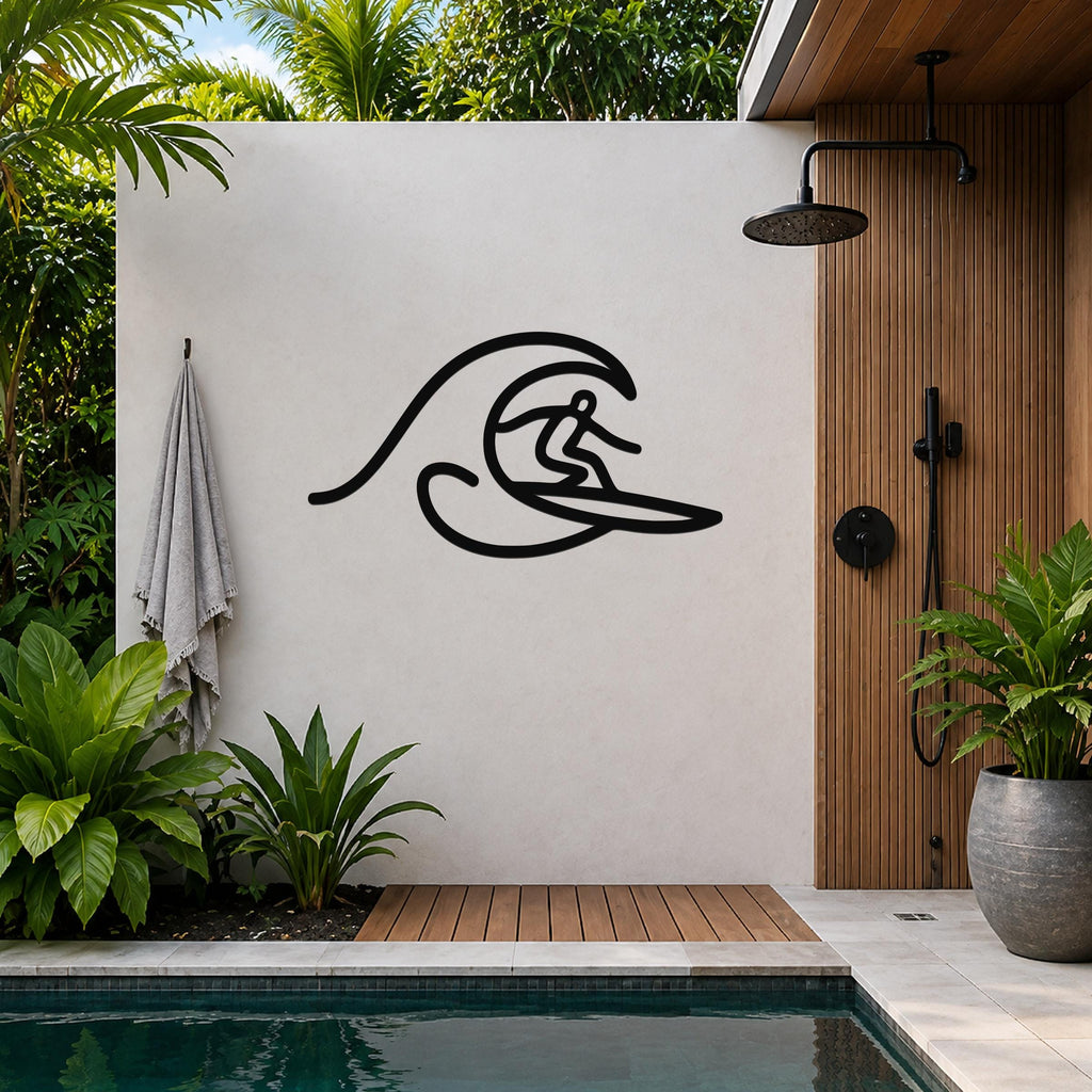 Black metal wall art silhouette of a surfer riding a wave, mounted on a light-colored outdoor wall beside a wooden shower enclosure and pool.
