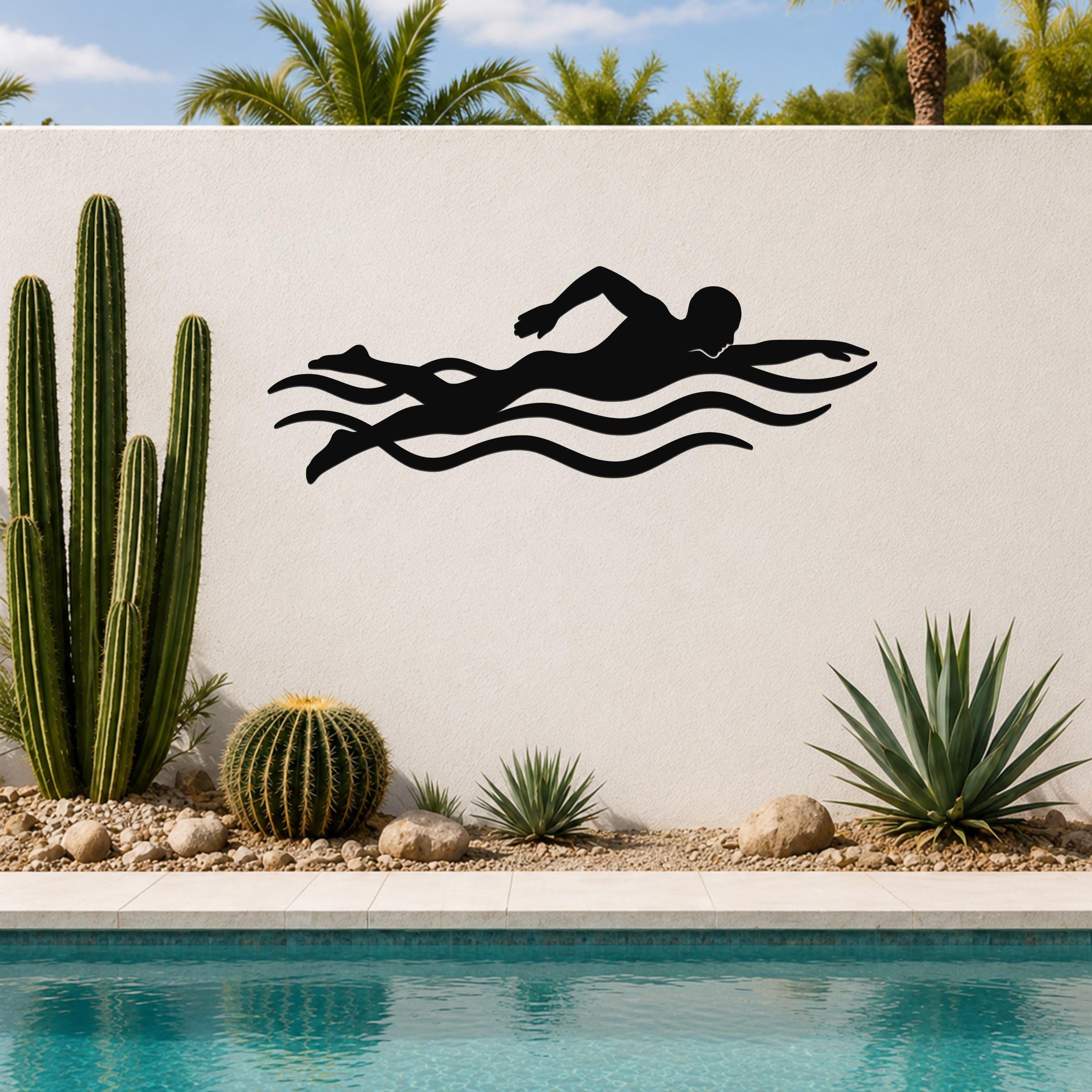 Black metal swimmer wall art with motion-line cutouts, mounted on an outdoor wall above a pool with cacti and palm trees in the background.