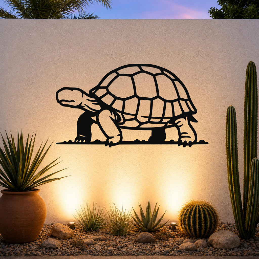 Black metal tortoise wall art with detailed shell cutouts, mounted on an outdoor wall above a desert garden with cacti and warm uplighting.