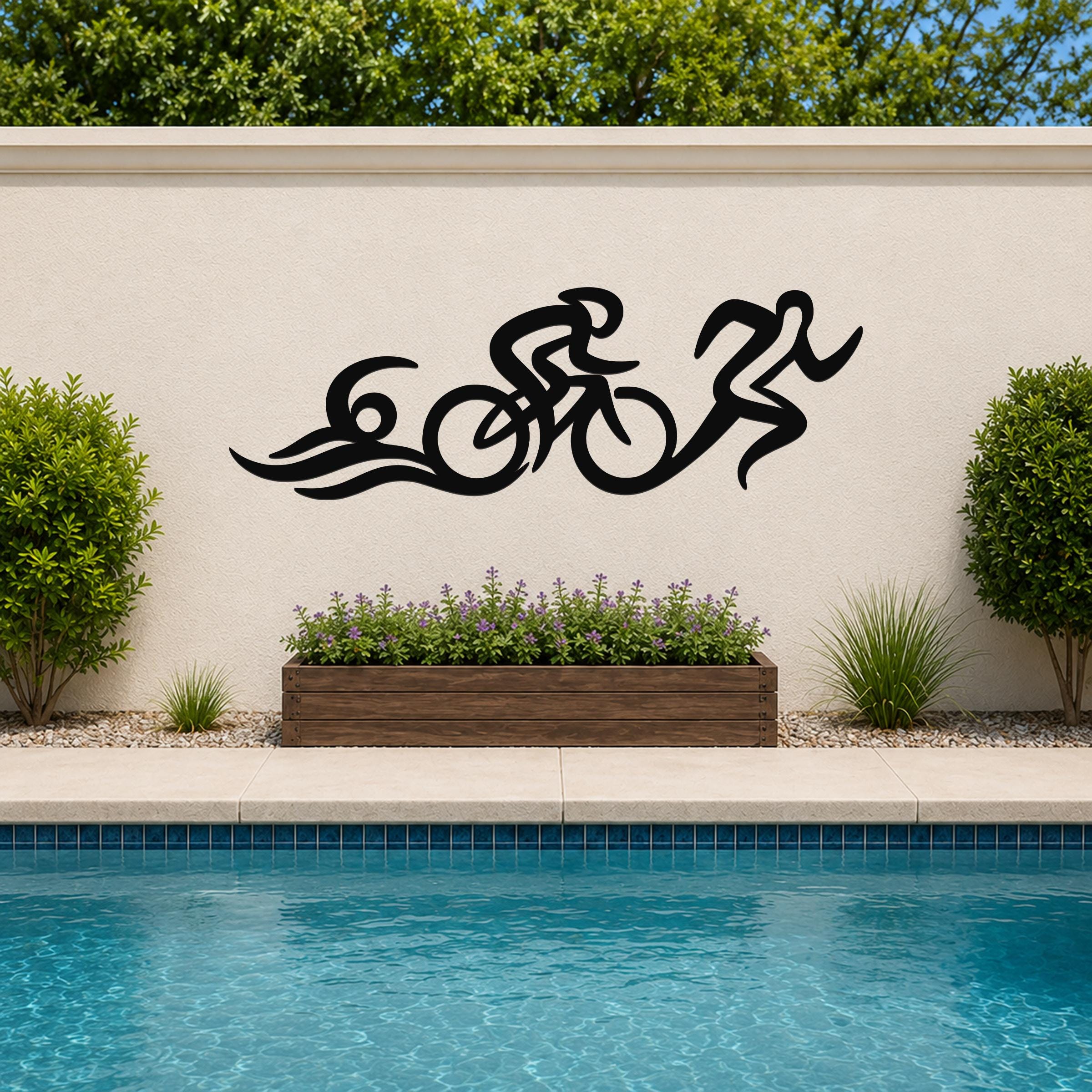 Black metal triathlon wall art with flowing cutout design of swim, bike, and run, mounted on an outdoor wall above a poolside planter.