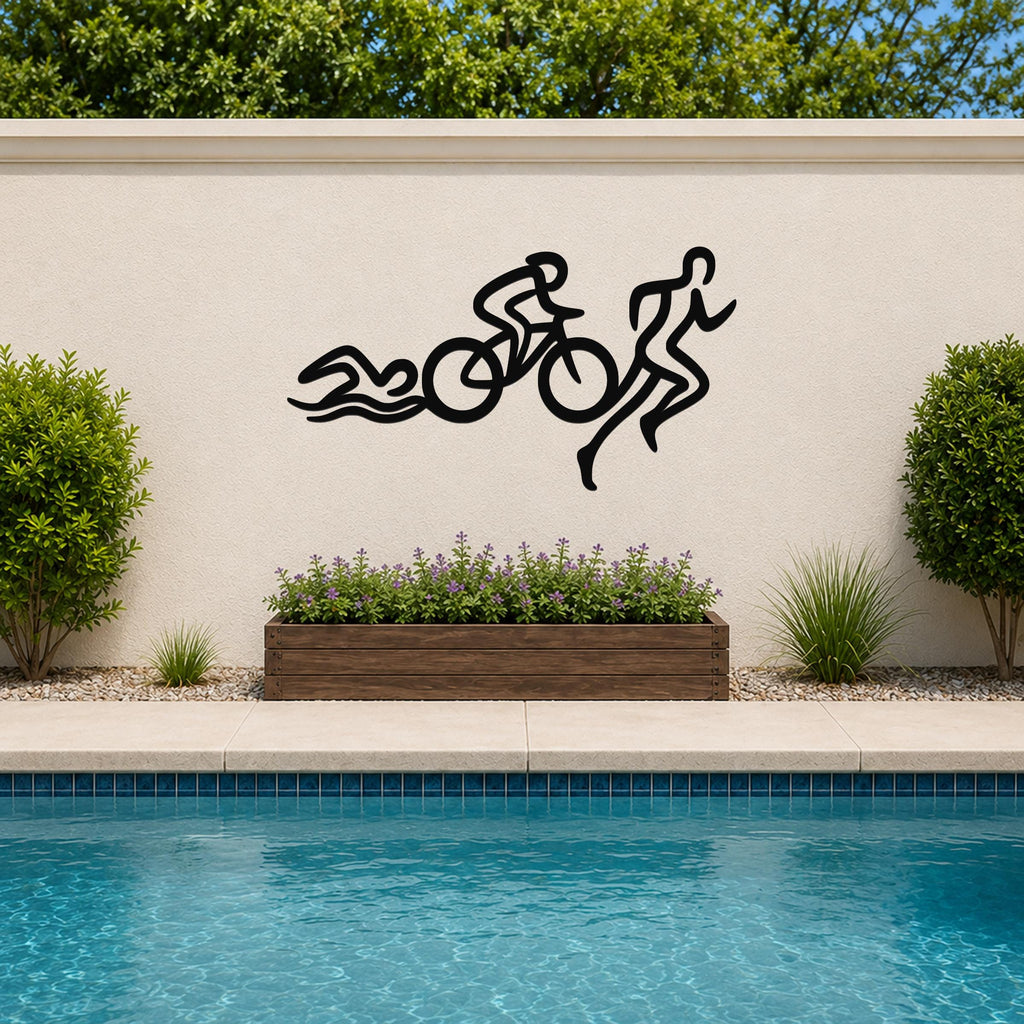 Black metal triathlon wall art with swim, bike, and run silhouette cutouts, mounted on an outdoor wall above a poolside planter.