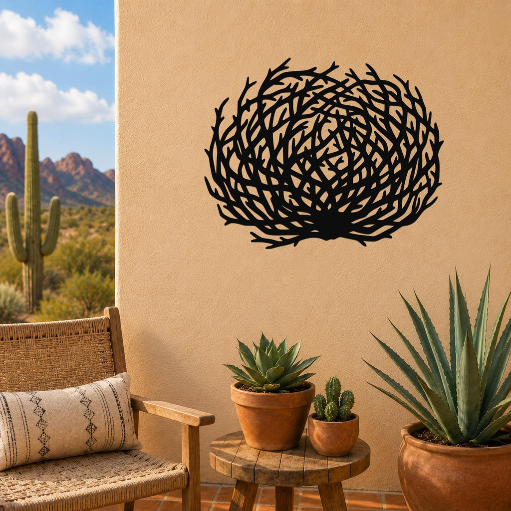 Black metal tumbleweed wall art with intricate branch cutouts, mounted on a tan outdoor wall above a small wooden table with potted succulents.