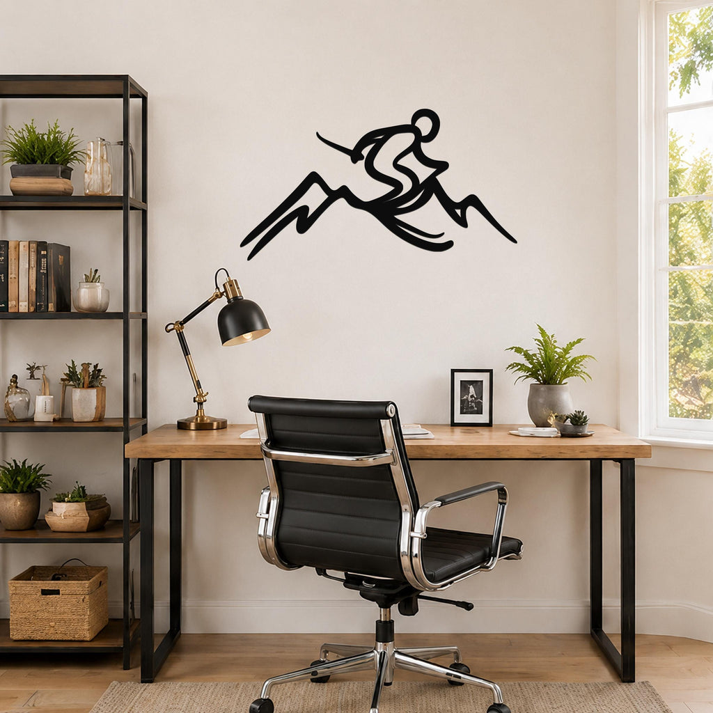 Black metal wall sculpture of a skier in motion above a mountain, mounted on a wall above a wooden desk in a home office.