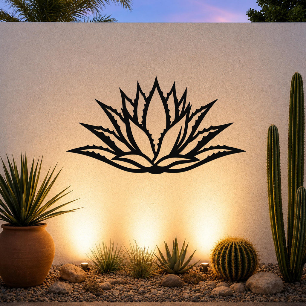 Black metal agave wall art with a bold geometric cutout design, mounted on an outdoor wall above a desert garden with cacti and warm ground lighting.