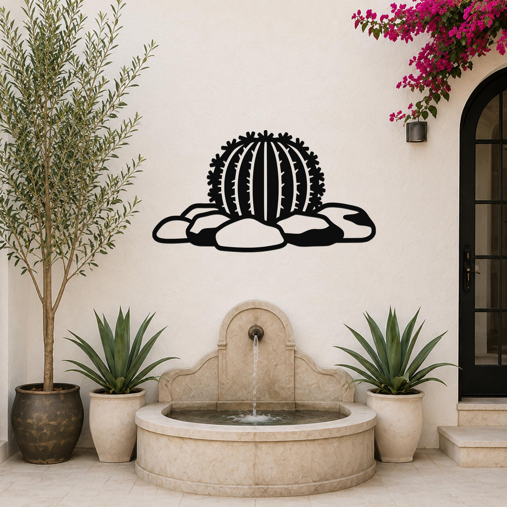 Black metal barrel cactus wall art with spines and rocks cutout, mounted on a white outdoor wall above a stone fountain.