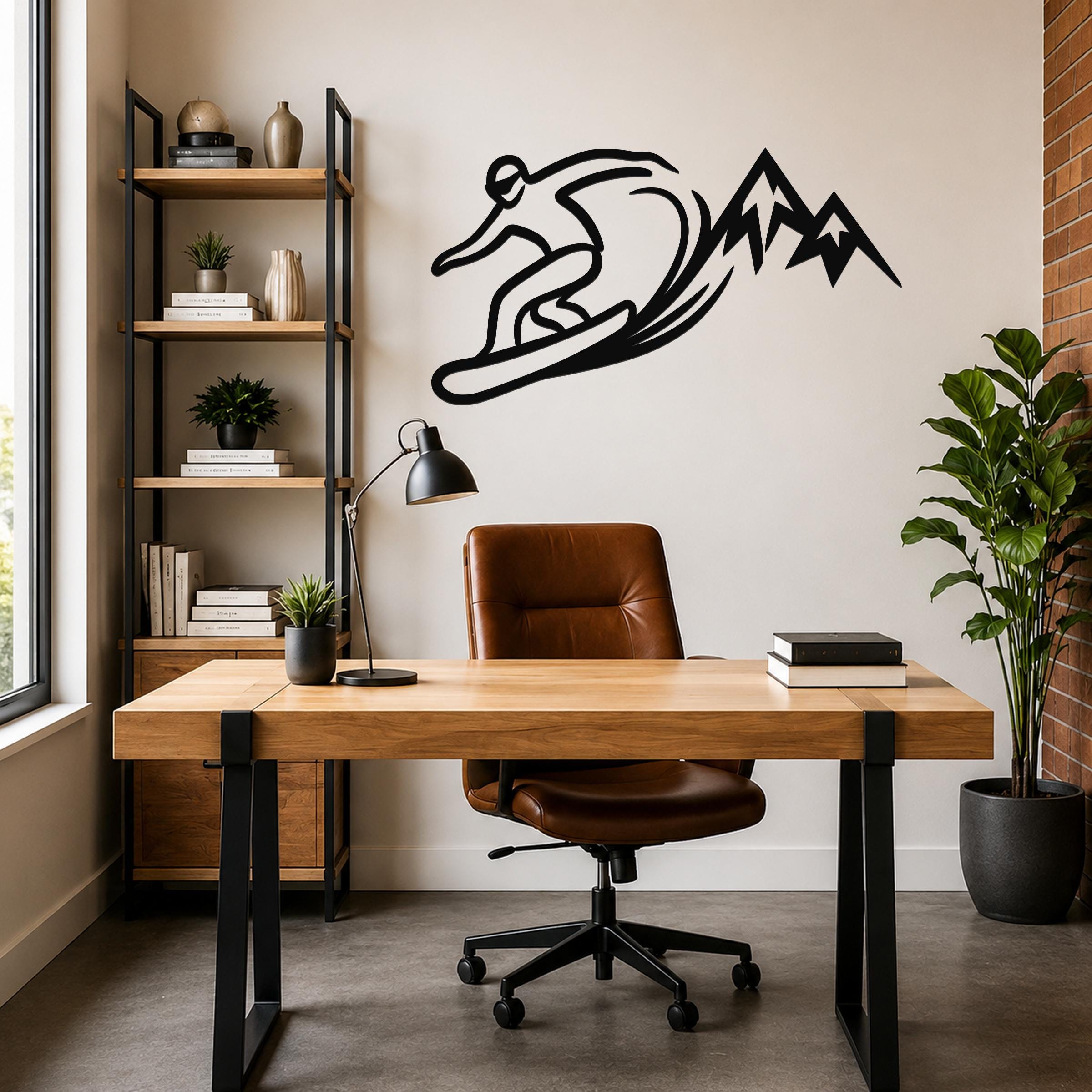 Black metal wall art silhouette of a snowboarder carving through powder with mountain peaks, mounted above a wooden desk in a modern home office.
