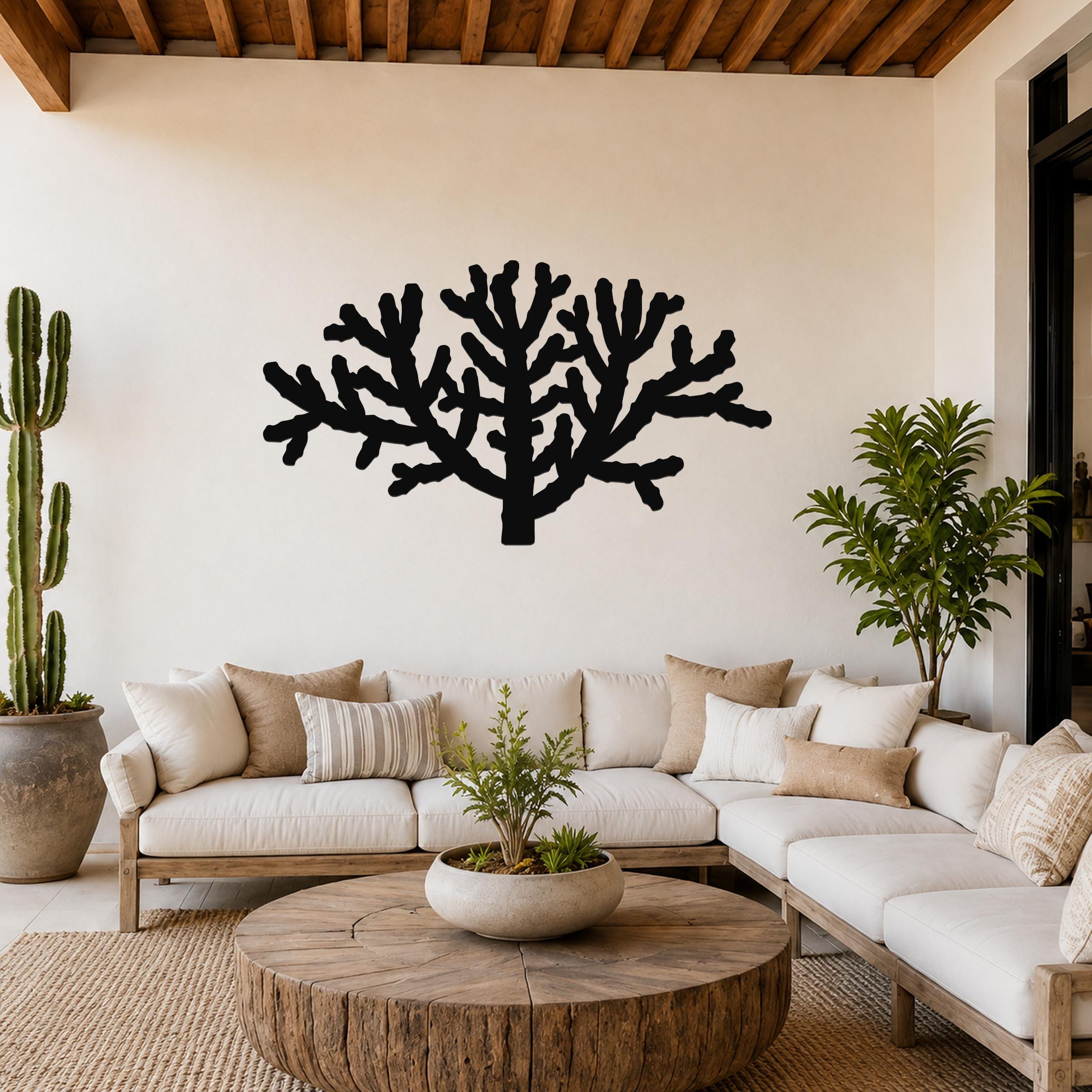 Black metal Cholla cactus wall art silhouette with branching cutouts, mounted on a living room wall above a white sofa.