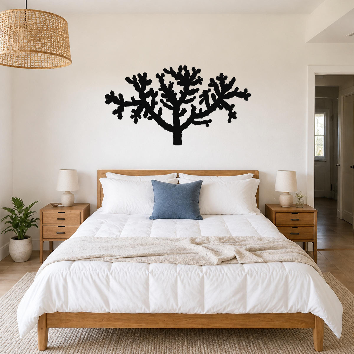Black metal Cholla cactus wall art silhouette with branching cutouts, mounted above a wooden bed in a bedroom.