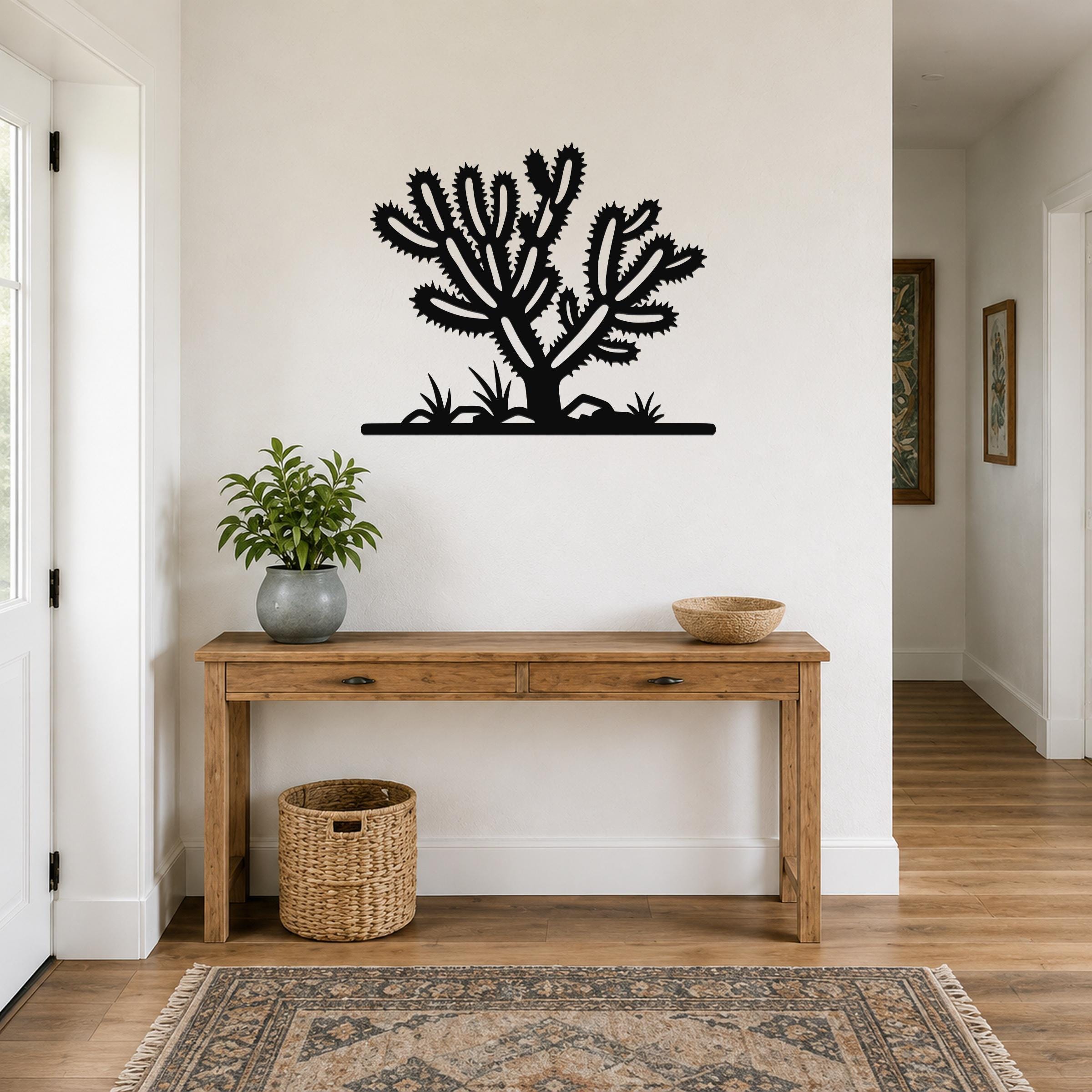 Black metal Cholla cactus wall art with spiky branch cutouts, mounted above a wooden console table in a hallway.