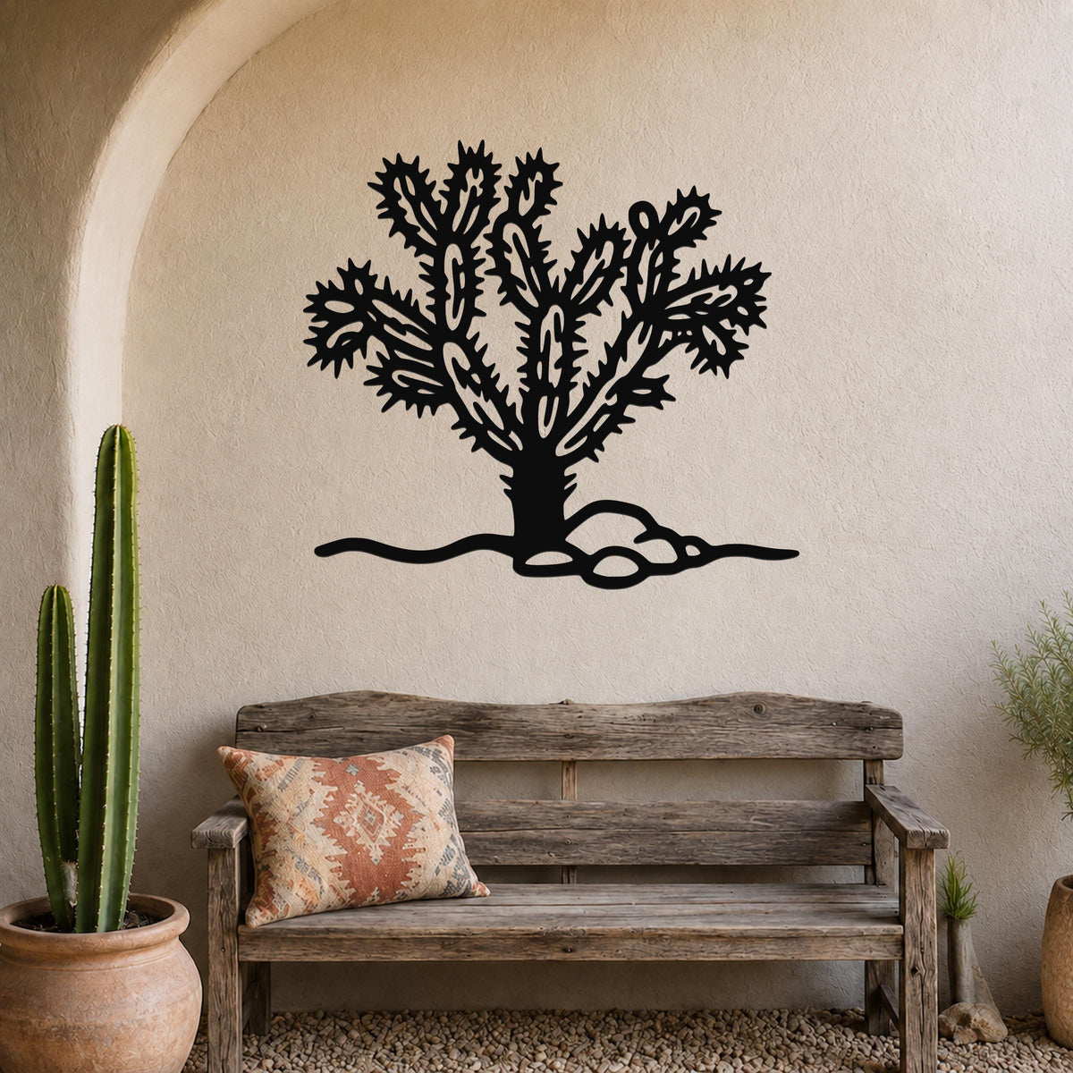 Black metal Cholla cactus wall art with intricate branch cutouts, mounted on a textured beige wall above a rustic wooden bench in a desert-themed entryway.