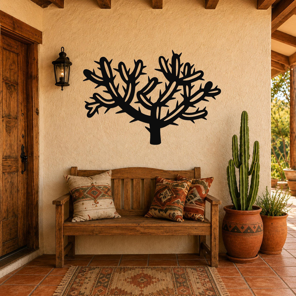 Black metal wall art in the silhouette of a cholla cactus with branching arms and spines, mounted on a stucco wall above a wooden bench in a patio entryway.