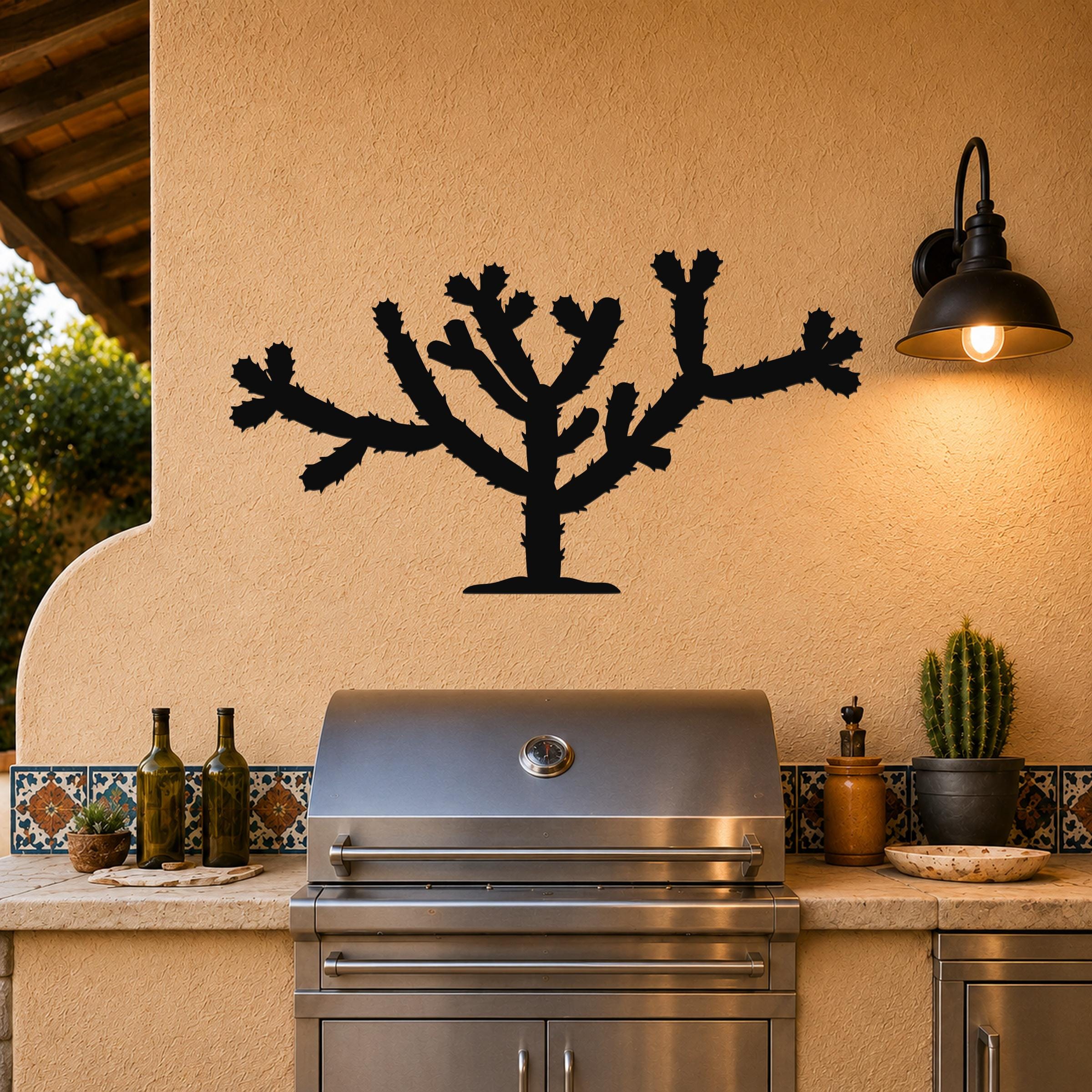 Black metal Cholla cactus wall art silhouette with spiny branches, mounted on a stucco outdoor wall above a stainless steel grill.