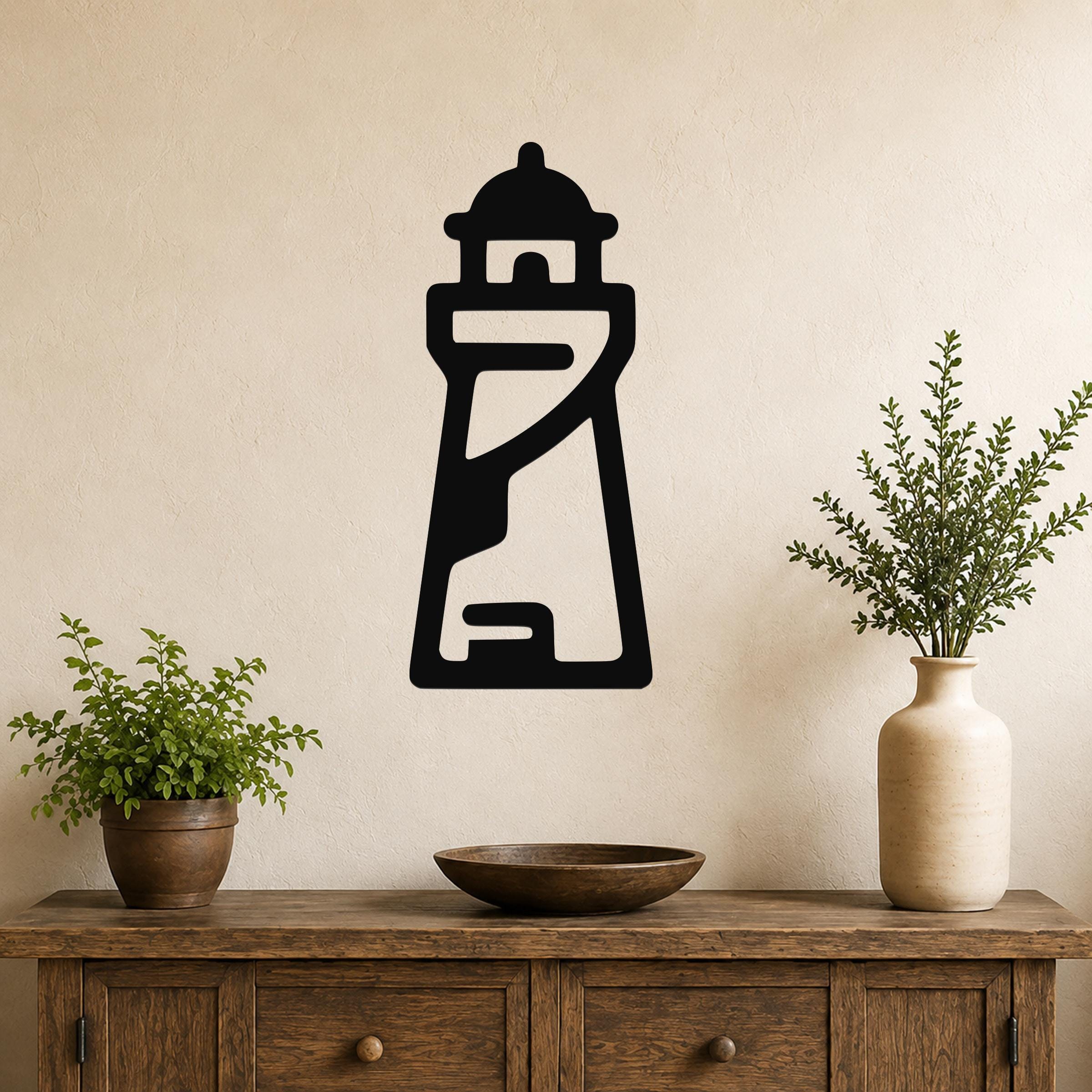 Black metal lighthouse wall art with internal cutout details, mounted on a beige wall above a wooden console table with plants.