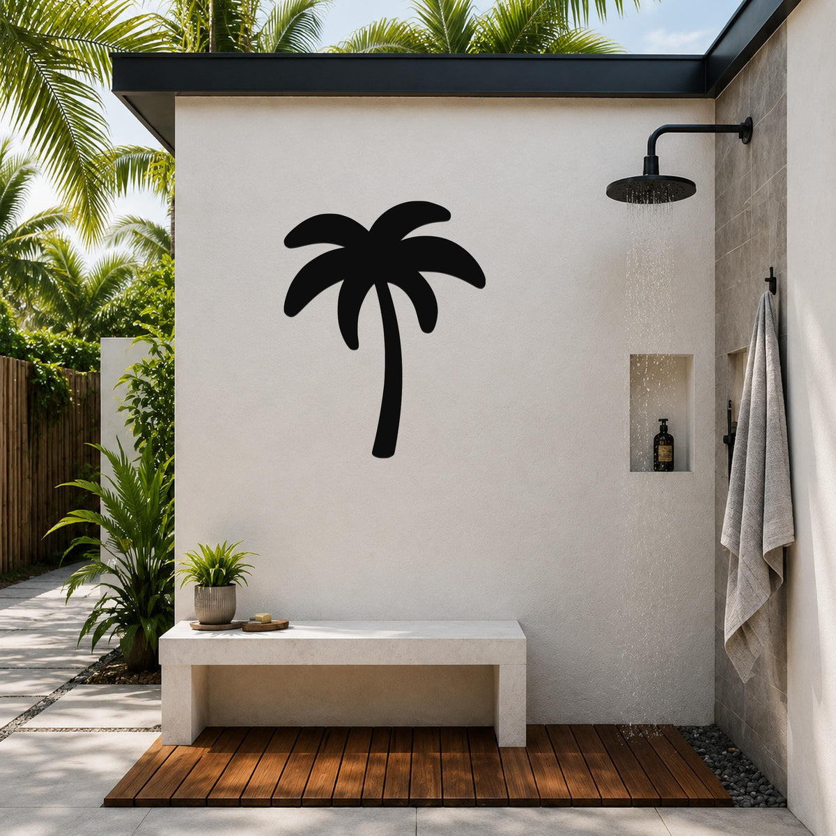 Black metal palm tree wall art silhouette mounted on a white outdoor shower wall, above a concrete bench in a tropical patio setting.