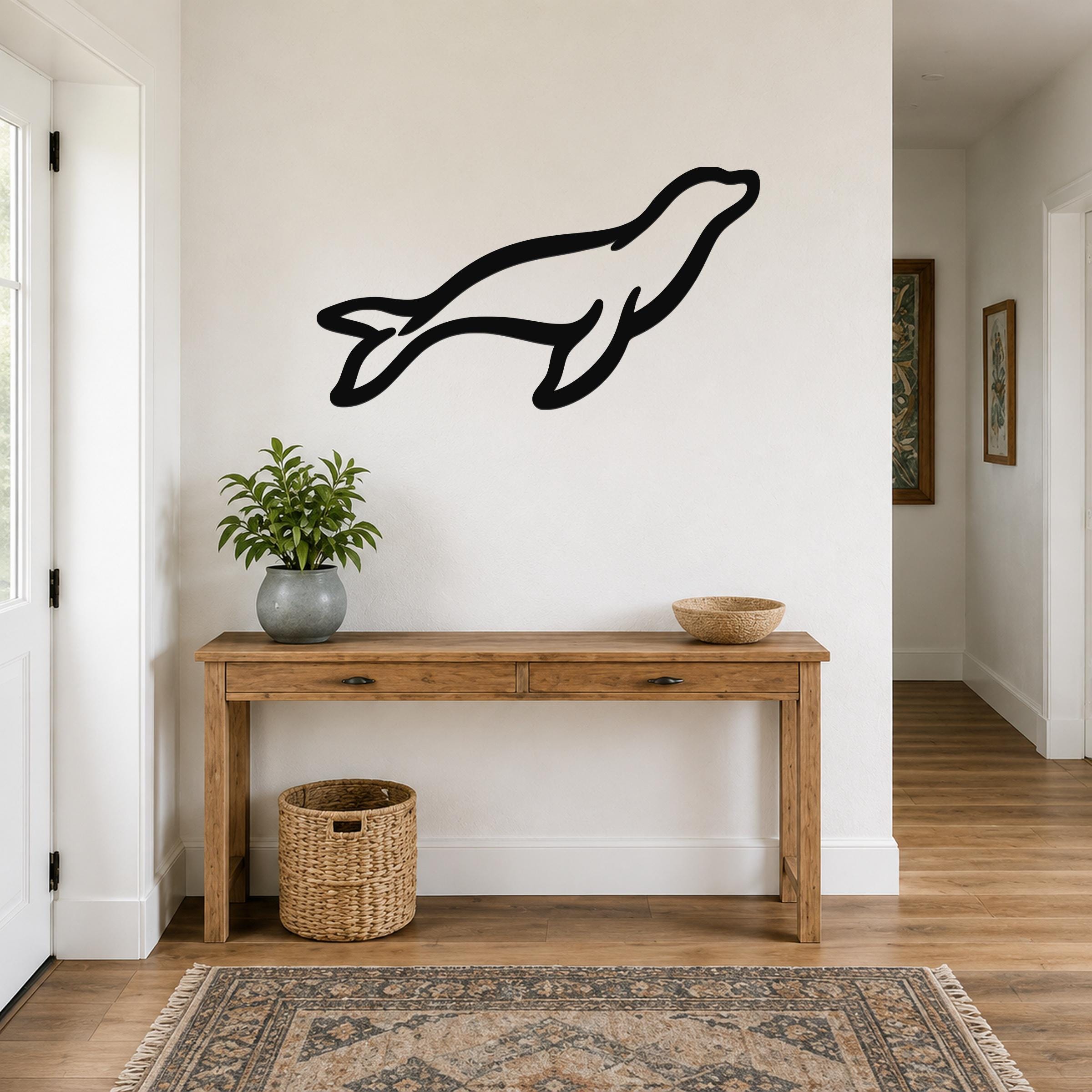 Black metal sea lion wall art silhouette mounted above a wooden console table in a bright entryway.