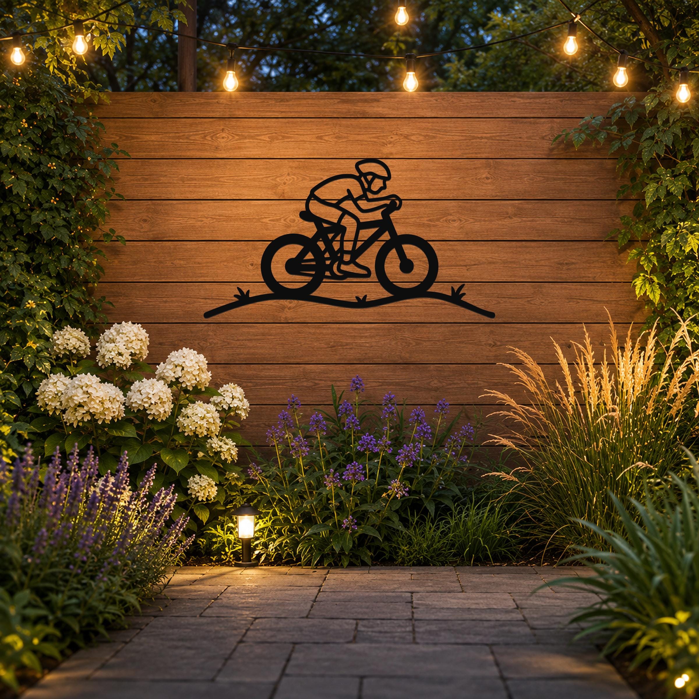 Black metal wall art featuring a minimalist cyclist silhouette on a bike with motion lines, mounted on a wooden outdoor wall above a garden with string lights and plants.
