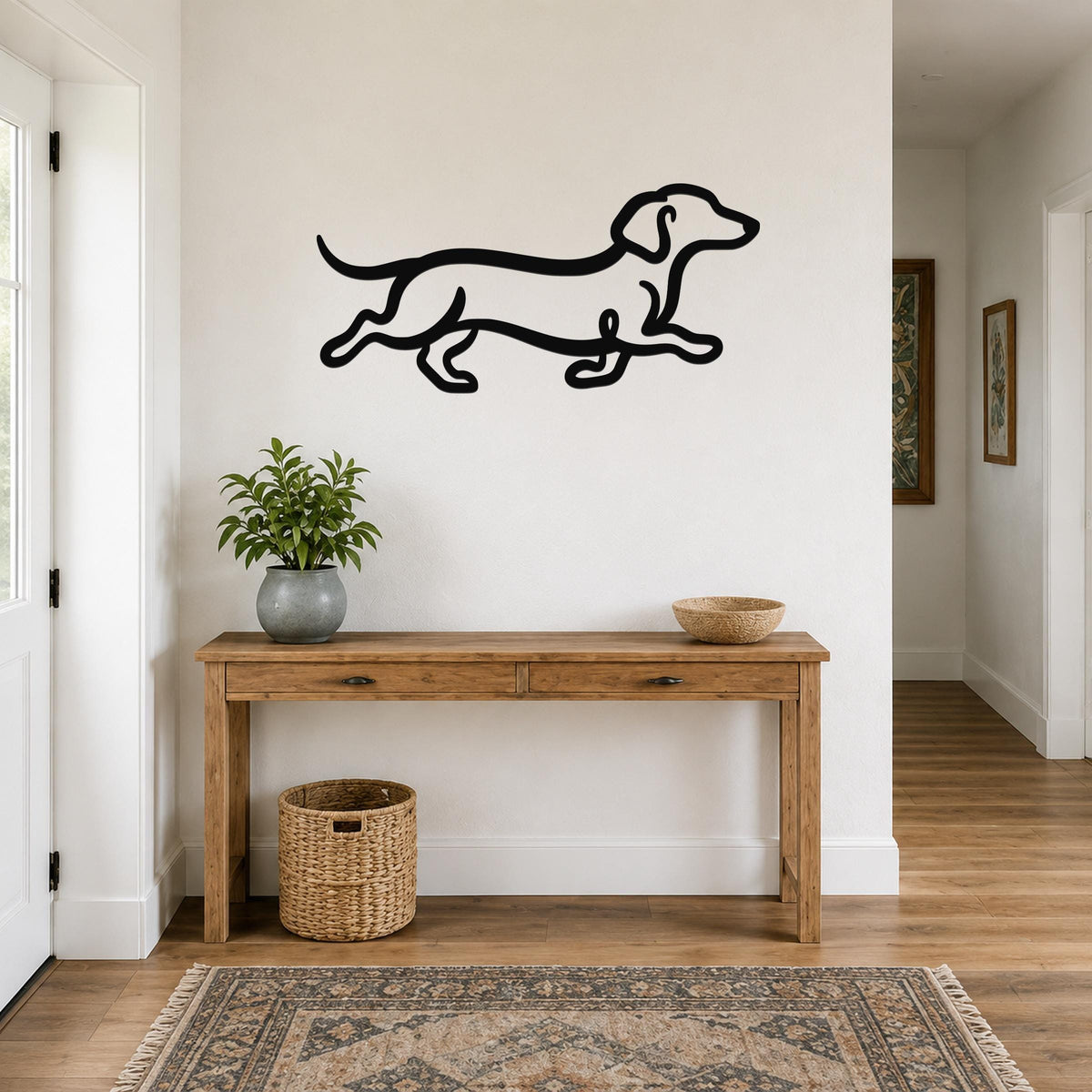 Black metal dachshund wall art with a continuous line silhouette, mounted above a wooden console table in a hallway.