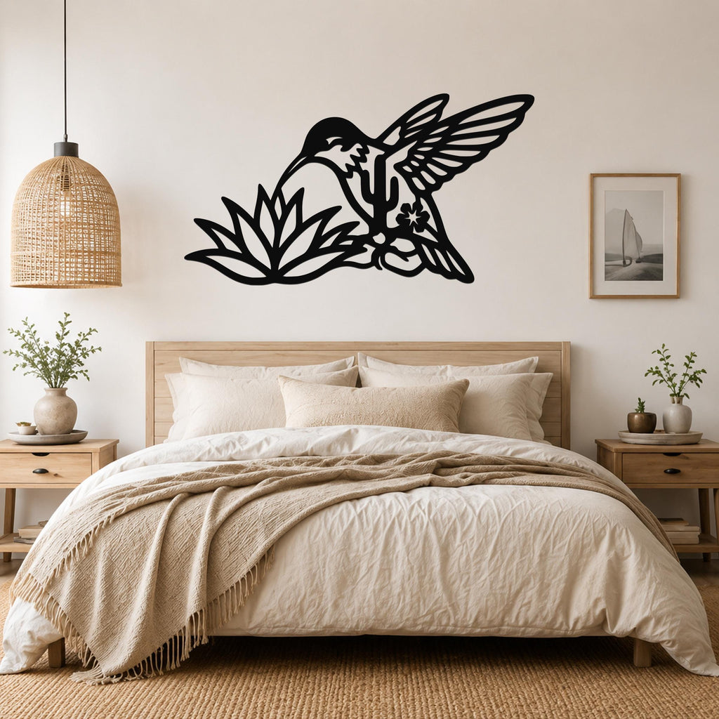 Black metal hummingbird wall art with cactus and flower cutouts, mounted above a bed in a neutral bedroom.