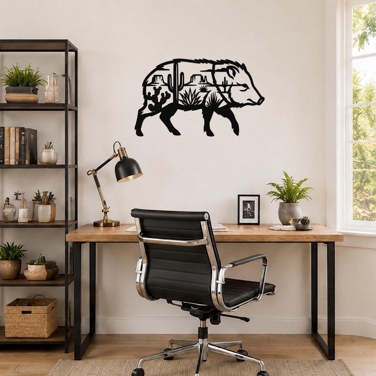 Black metal wall art in the silhouette of a javelina, with desert landscape cutouts including cacti and mountains, mounted on a wall above a wooden desk in a home office.