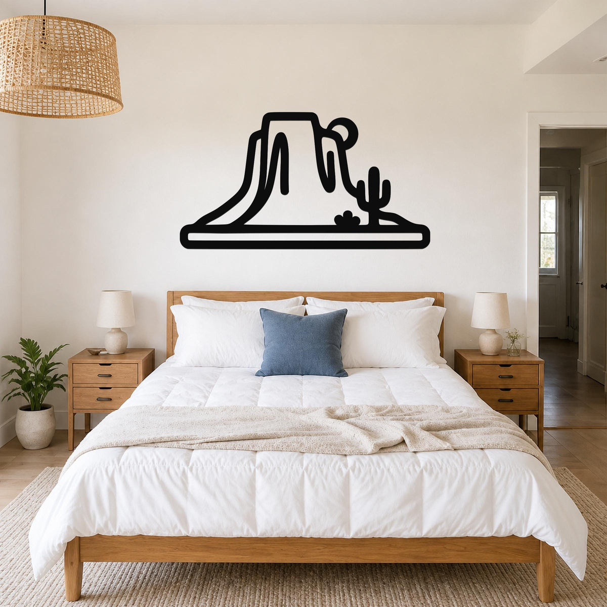 Black metal wall art silhouette of a desert mesa and cactus, mounted above a bed in a bedroom.