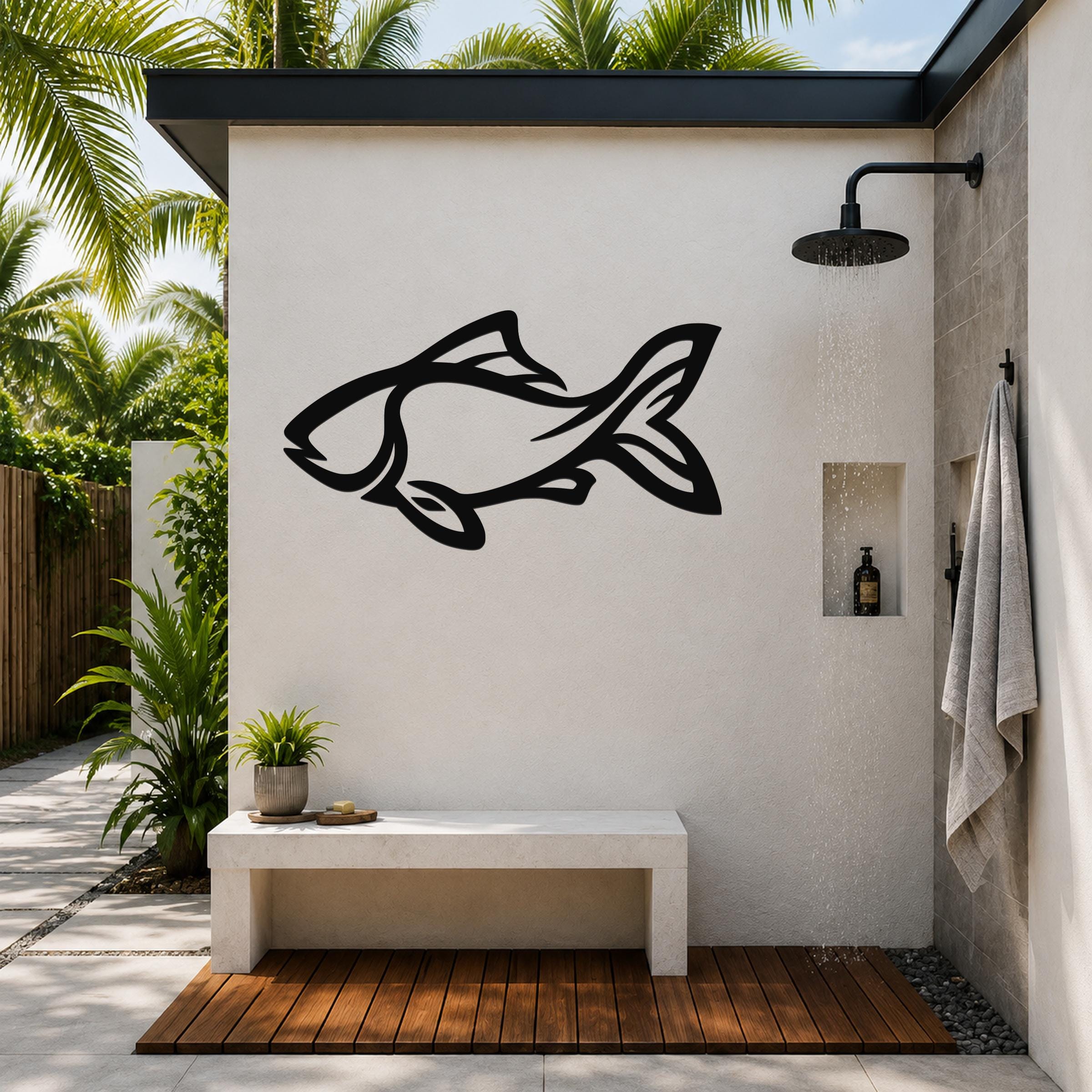 Black metal fish wall art with internal cutout details, mounted on a white outdoor shower wall above a concrete bench.