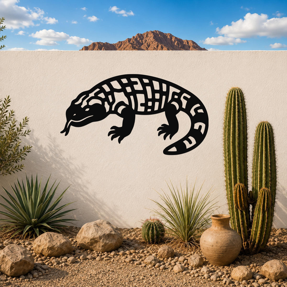 Black metal Gila monster wall art with geometric cutout patterns, mounted on a white outdoor wall above a desert garden with cacti and rocks.