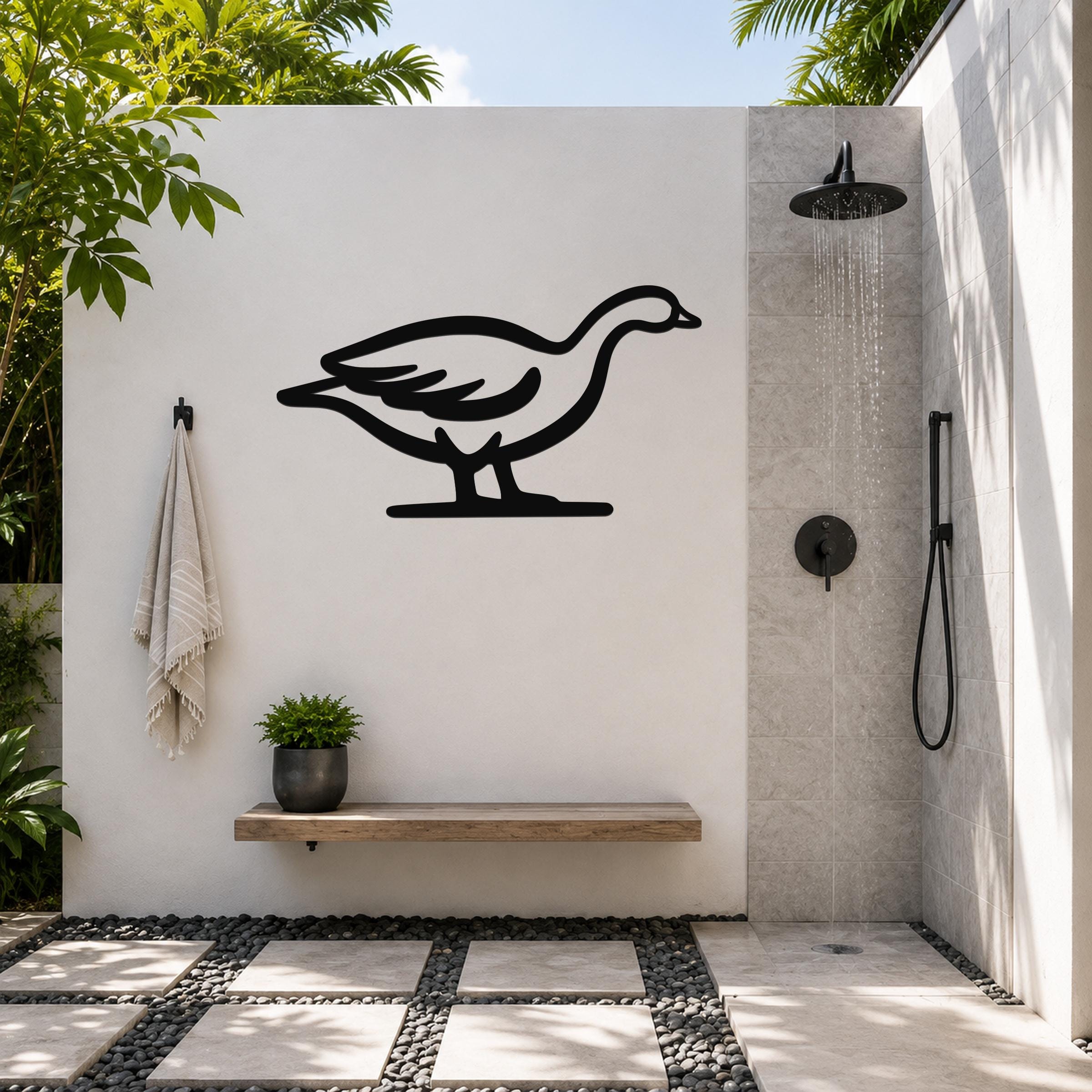 Black metal goose wall art silhouette mounted on a white outdoor shower wall, above a wooden bench with a potted plant.