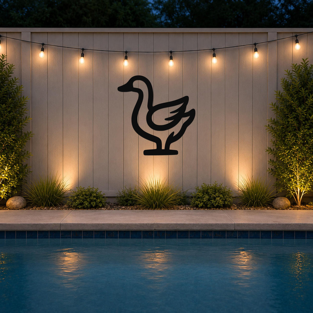 Black metal goose silhouette wall art mounted on a light-colored outdoor fence above a pool, illuminated by string lights at dusk.