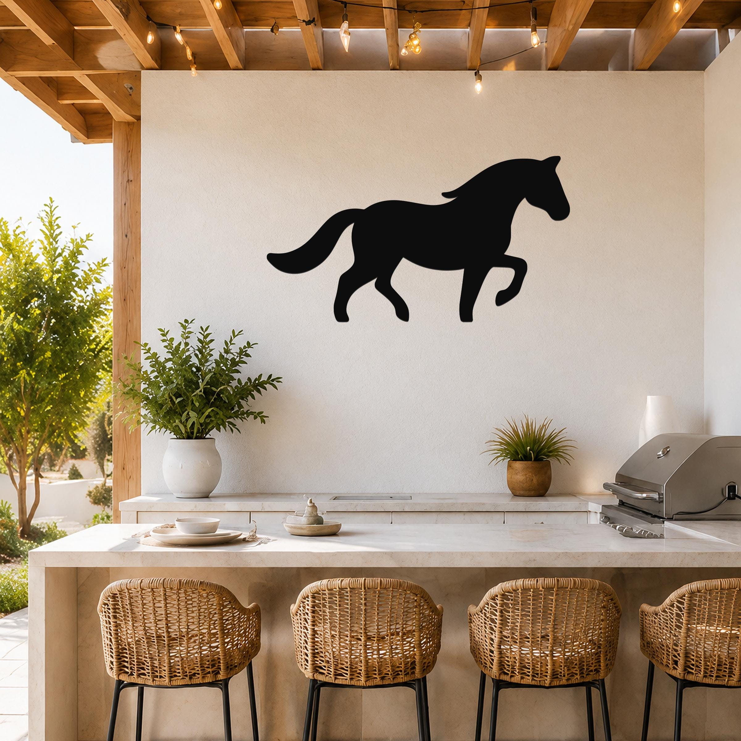 Black metal horse silhouette wall art mounted on a white wall above a kitchen counter with wicker bar stools and string lights.