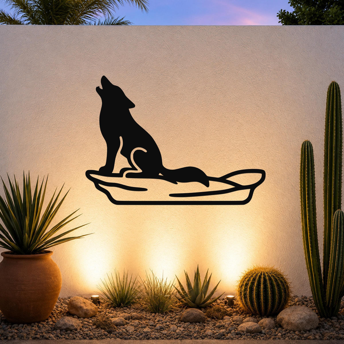Black metal coyote wall art in a howling silhouette, mounted on an outdoor wall above a desert garden with cacti and warm uplighting.