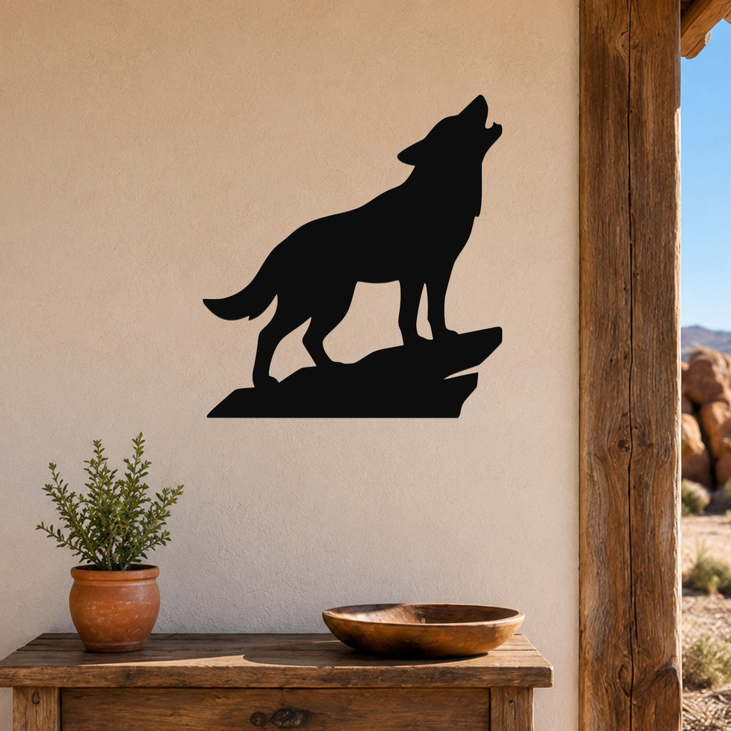 Black metal coyote wall art silhouette howling on a rock, mounted on a beige wall above a wooden table with a potted plant and bowl.