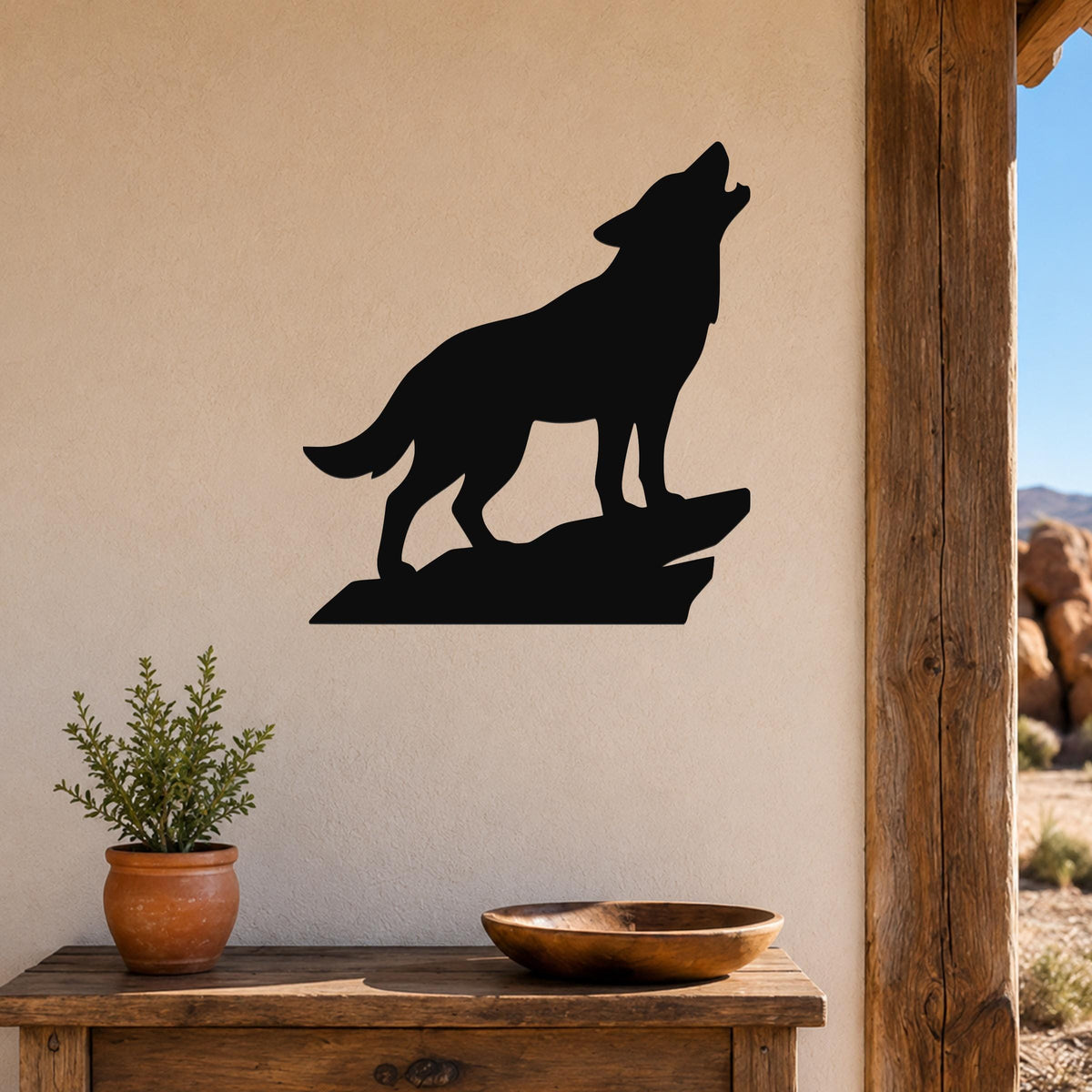 Black metal coyote wall art silhouette howling on a rock, mounted on a beige wall above a wooden table with a potted plant and bowl.