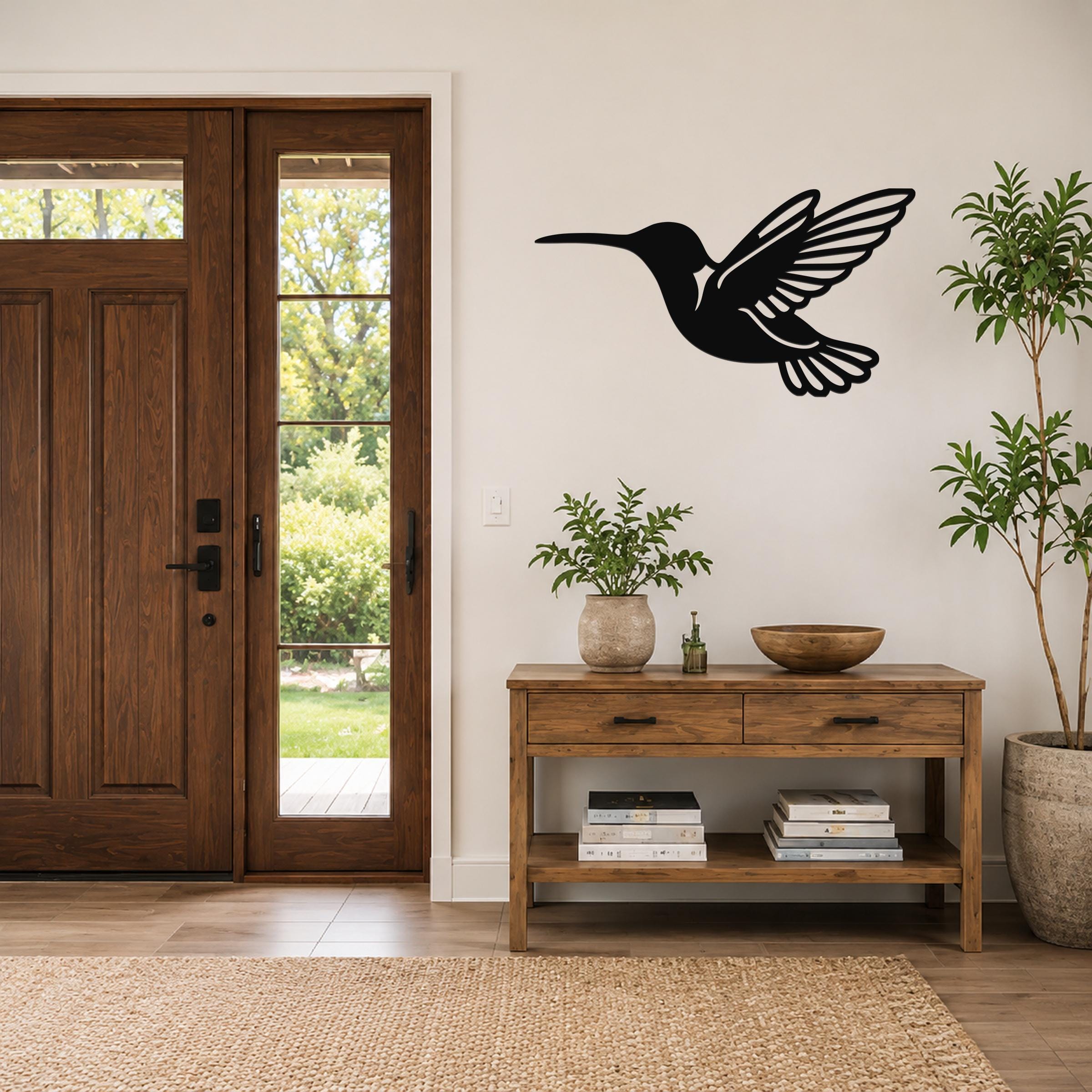 Black metal hummingbird wall art with wing and tail cutouts, mounted on a wall above a wooden console table in a entryway.
