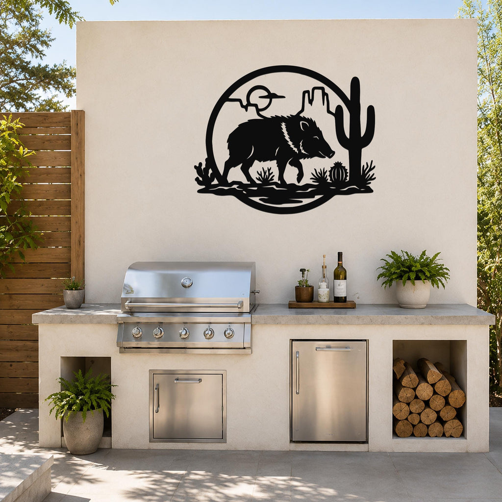 Black metal wall art featuring a javelina silhouette with cactus and desert landscape cutouts, mounted on an outdoor kitchen wall above a stainless steel grill.