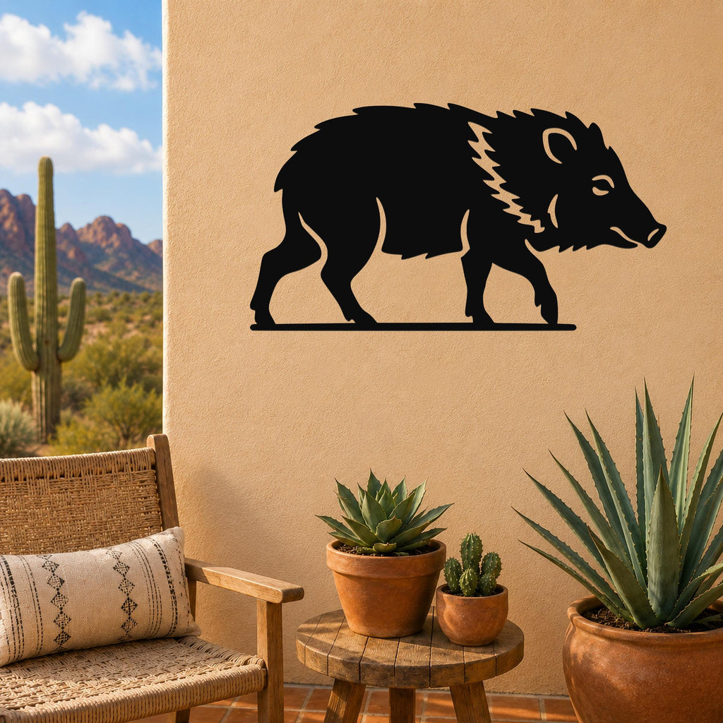 Black metal javelina wall art silhouette with internal cutout details, mounted on a tan outdoor wall above a small wooden table with potted succulents.