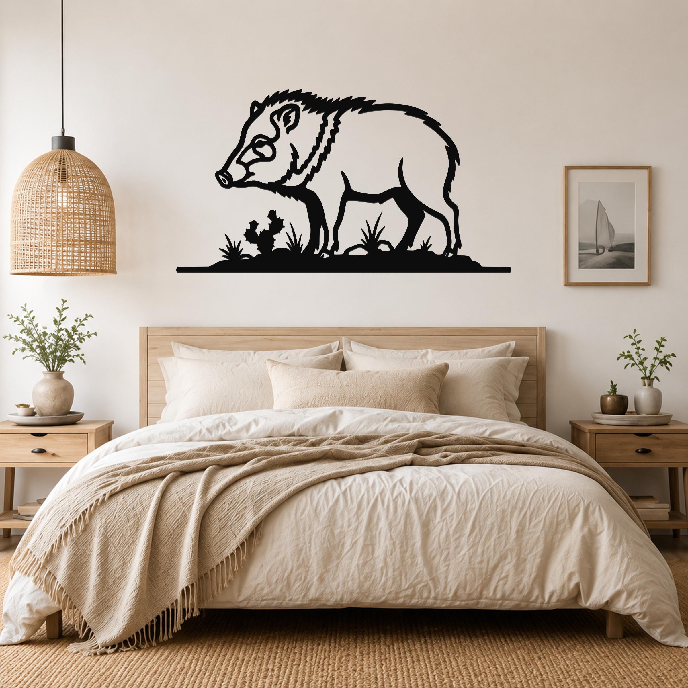 Black metal javelina wall art with grass and cactus cutouts, mounted above a bed in a neutral bedroom.