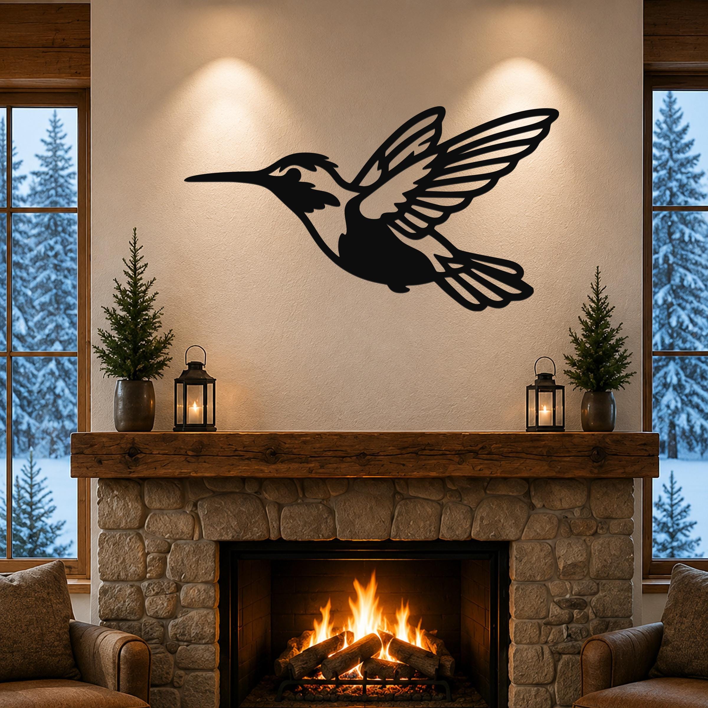 Black metal hummingbird wall art with open wings and internal cutout details, mounted above a stone fireplace in a living room.