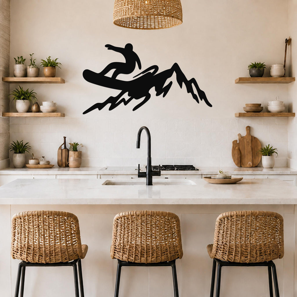 Black metal wall art silhouette of a snowboarder on a mountain, mounted above a kitchen counter with wicker bar stools and open shelves.