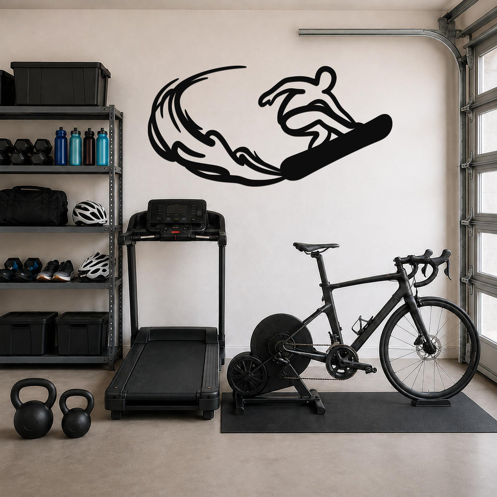 Black metal wall art silhouette of a snowboarder in motion with wave-like cutouts, mounted on a garage wall above a treadmill and bicycle.