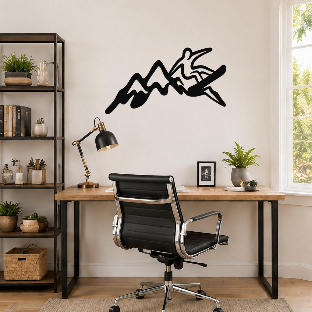 Black metal wall art silhouette of a snowboarder in motion over mountain peaks, mounted above a wooden desk in a home office.