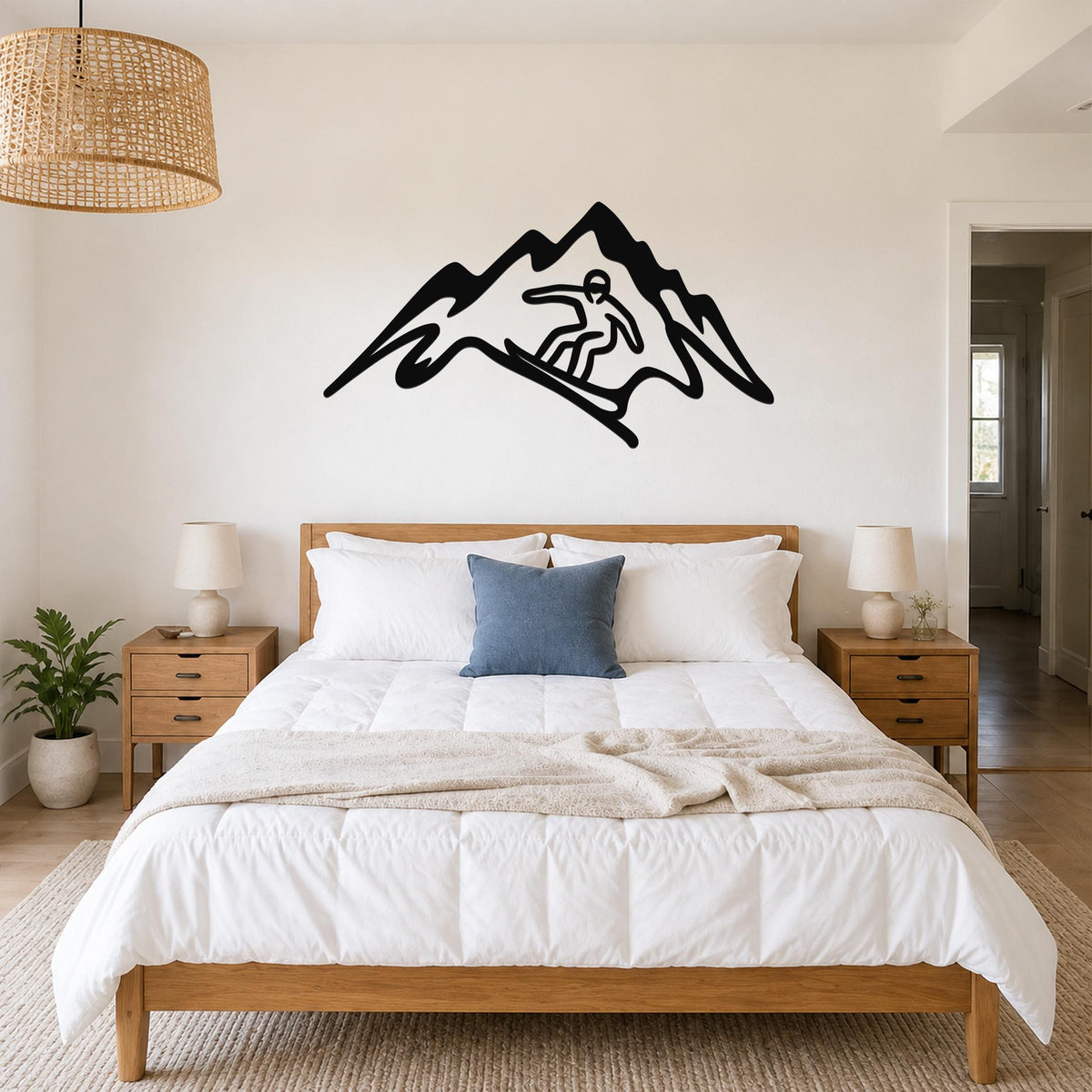Black metal wall art featuring a snowboarder silhouette within a mountain outline, mounted above a bed in a bedroom.