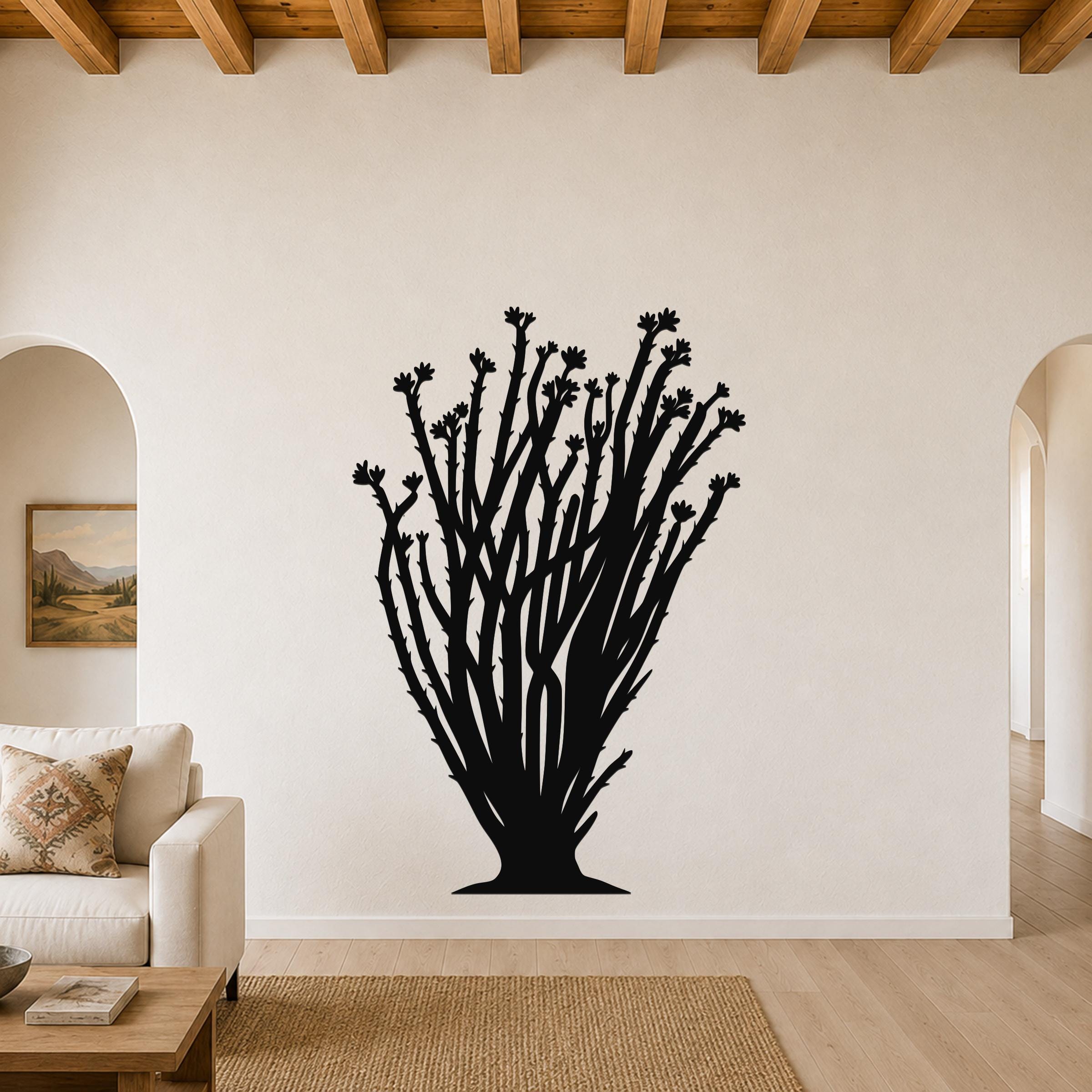 Black metal ocotillo wall art with branching stems and flower cutouts, mounted on a living room wall above a sofa.