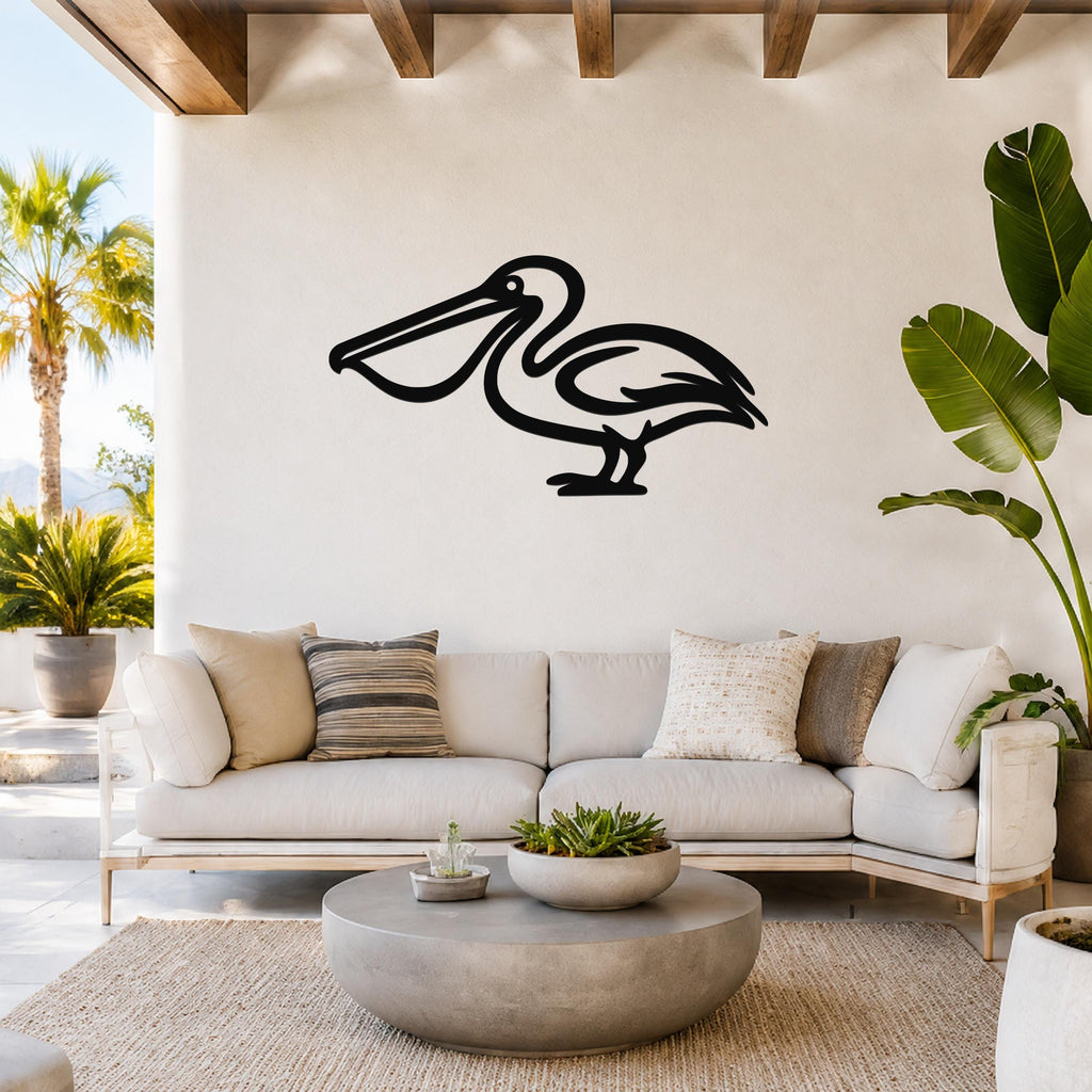 Black metal pelican wall art silhouette mounted above a white sofa in a bright living room with tropical plants and wooden beams.