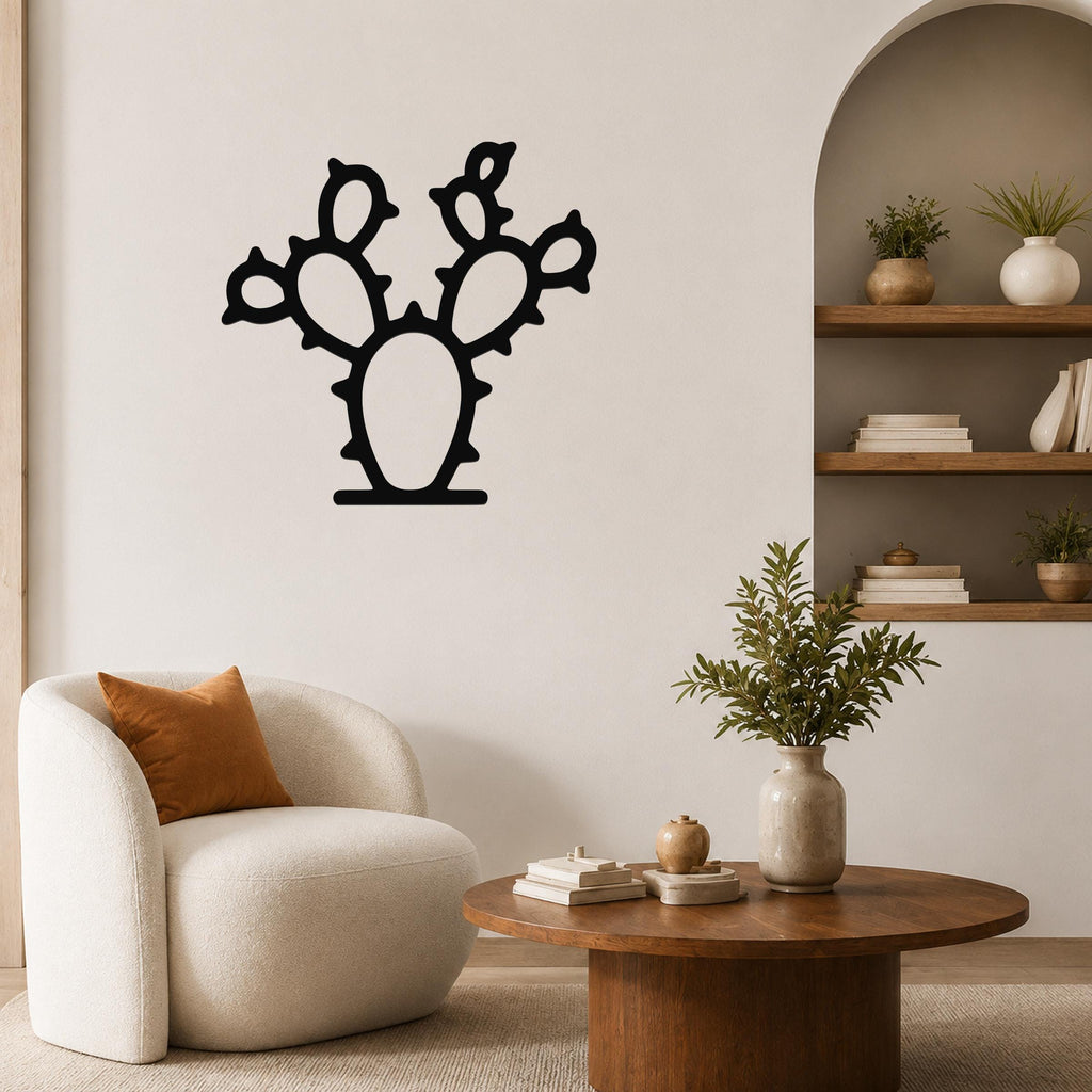 Black metal prickly pear cactus wall art with cutout pads and spines, mounted on a living room wall above a white armchair.