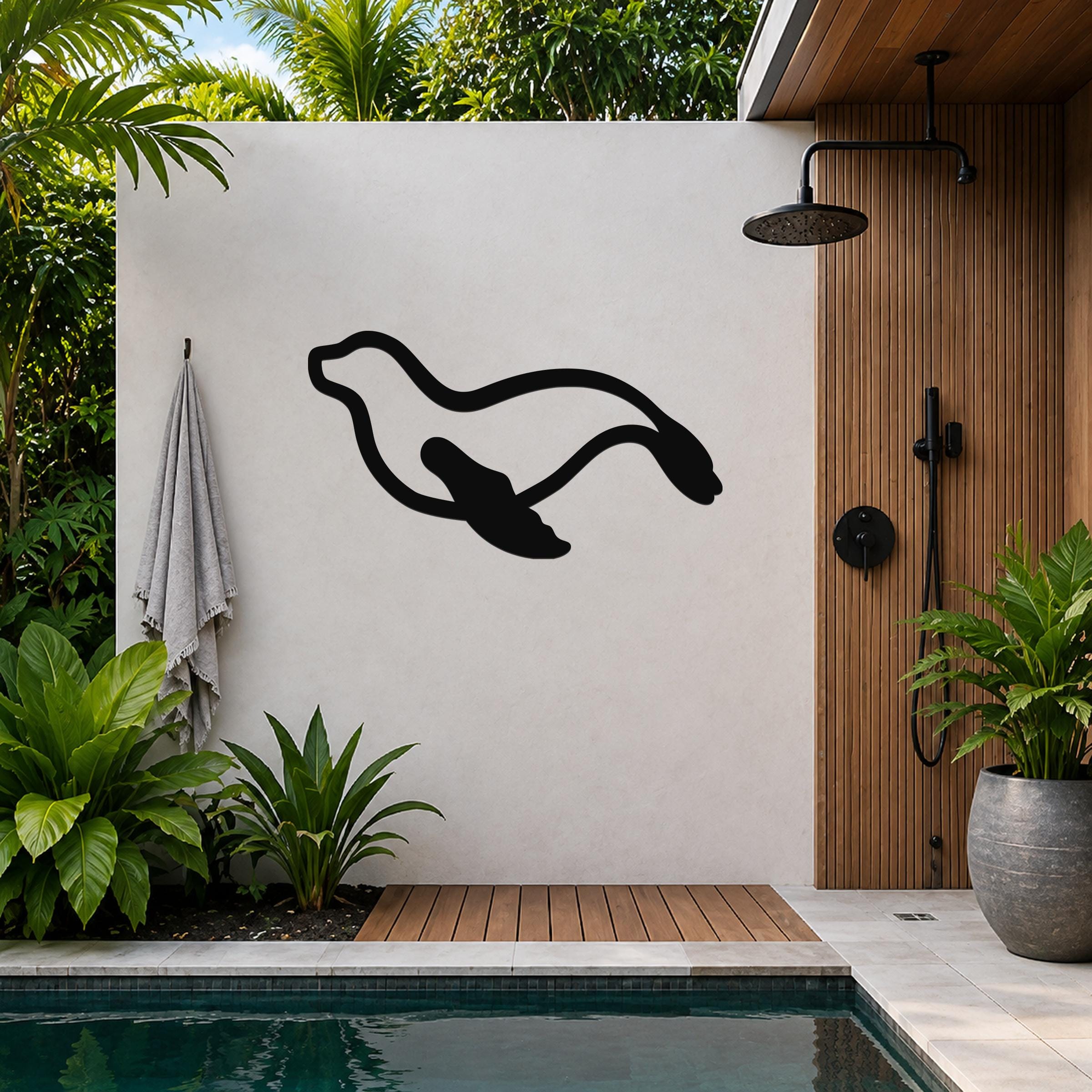 Black metal sea lion wall art silhouette mounted on a white outdoor wall beside a wooden shower and pool area.