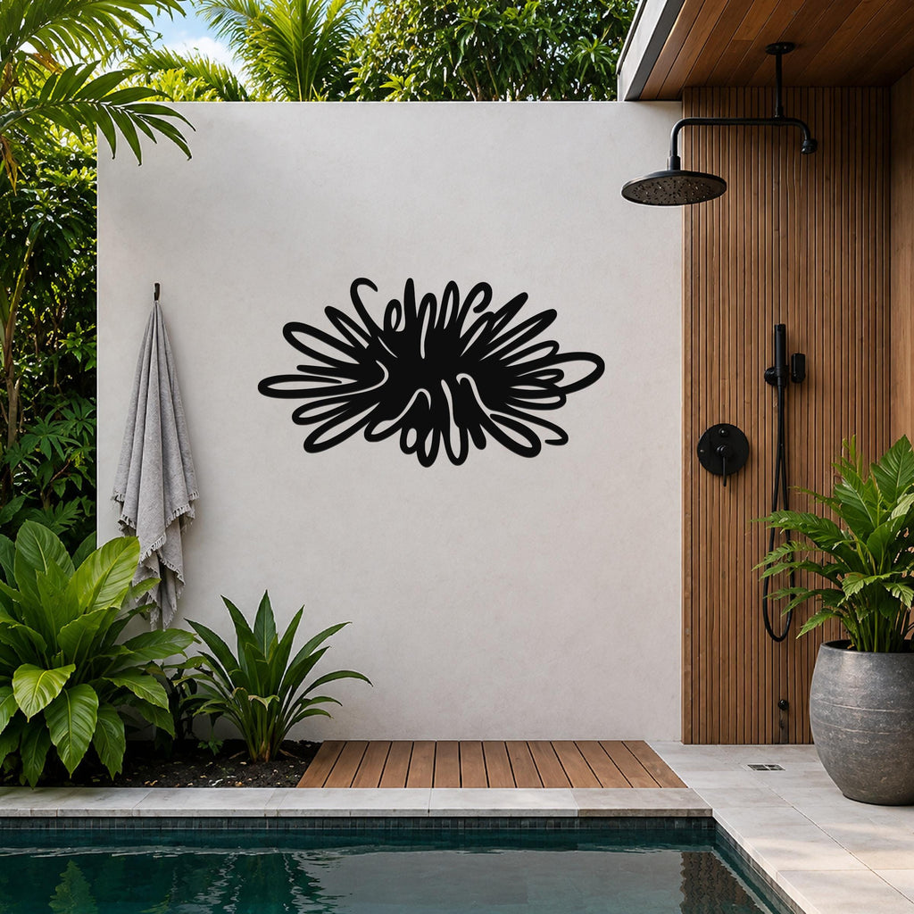 Black metal sea urchin wall art with spiky, radiating cutouts, mounted on a light-colored outdoor wall beside a wooden shower and pool area.