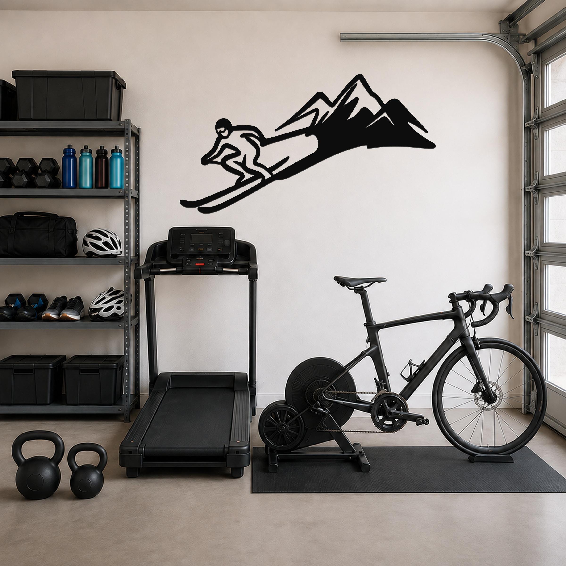 Black metal skier and mountain wall art silhouette mounted on a garage wall above a treadmill and bicycle.