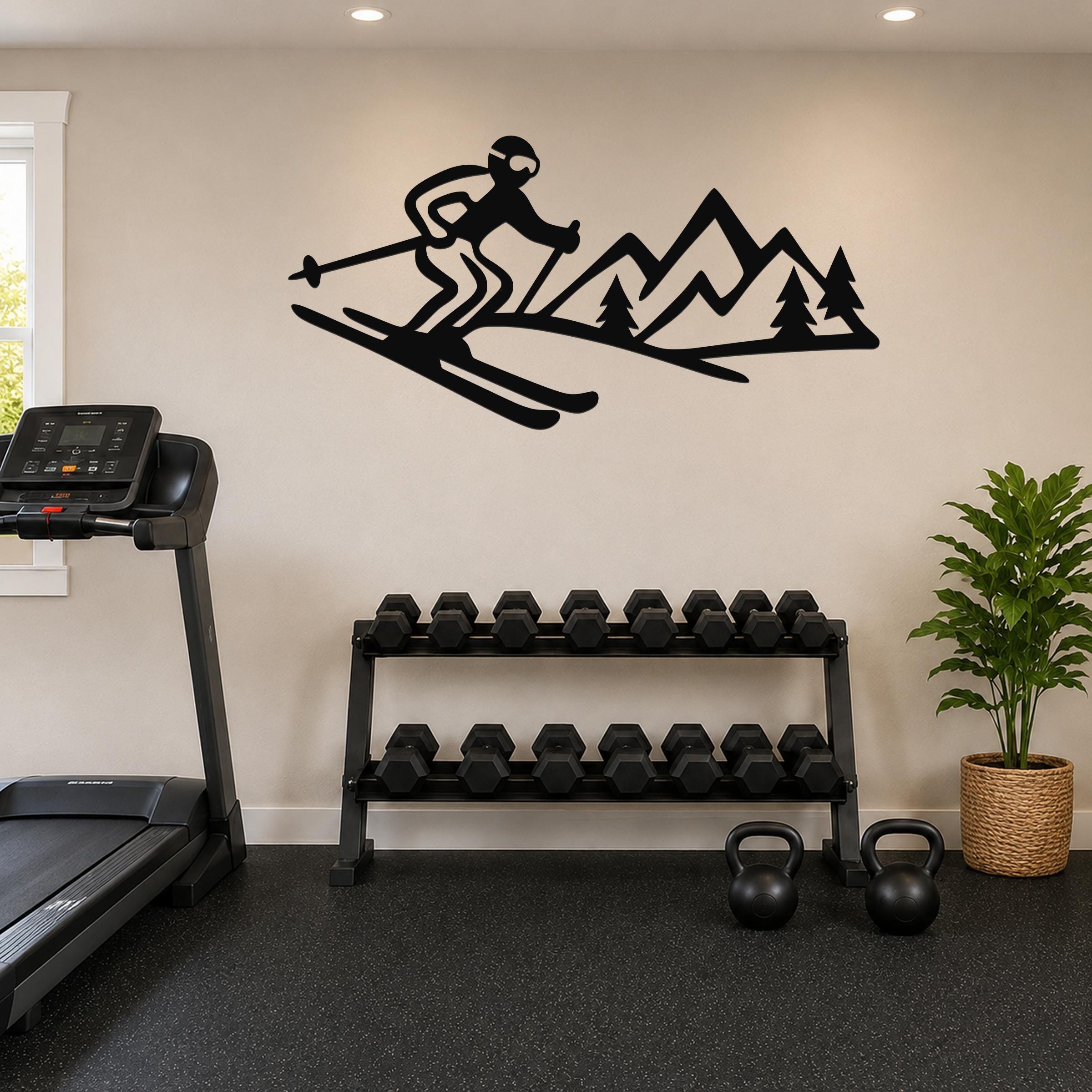 Black metal wall art cutout of a skier and mountain range with pine trees, mounted on a wall above a dumbbell rack in a home gym.