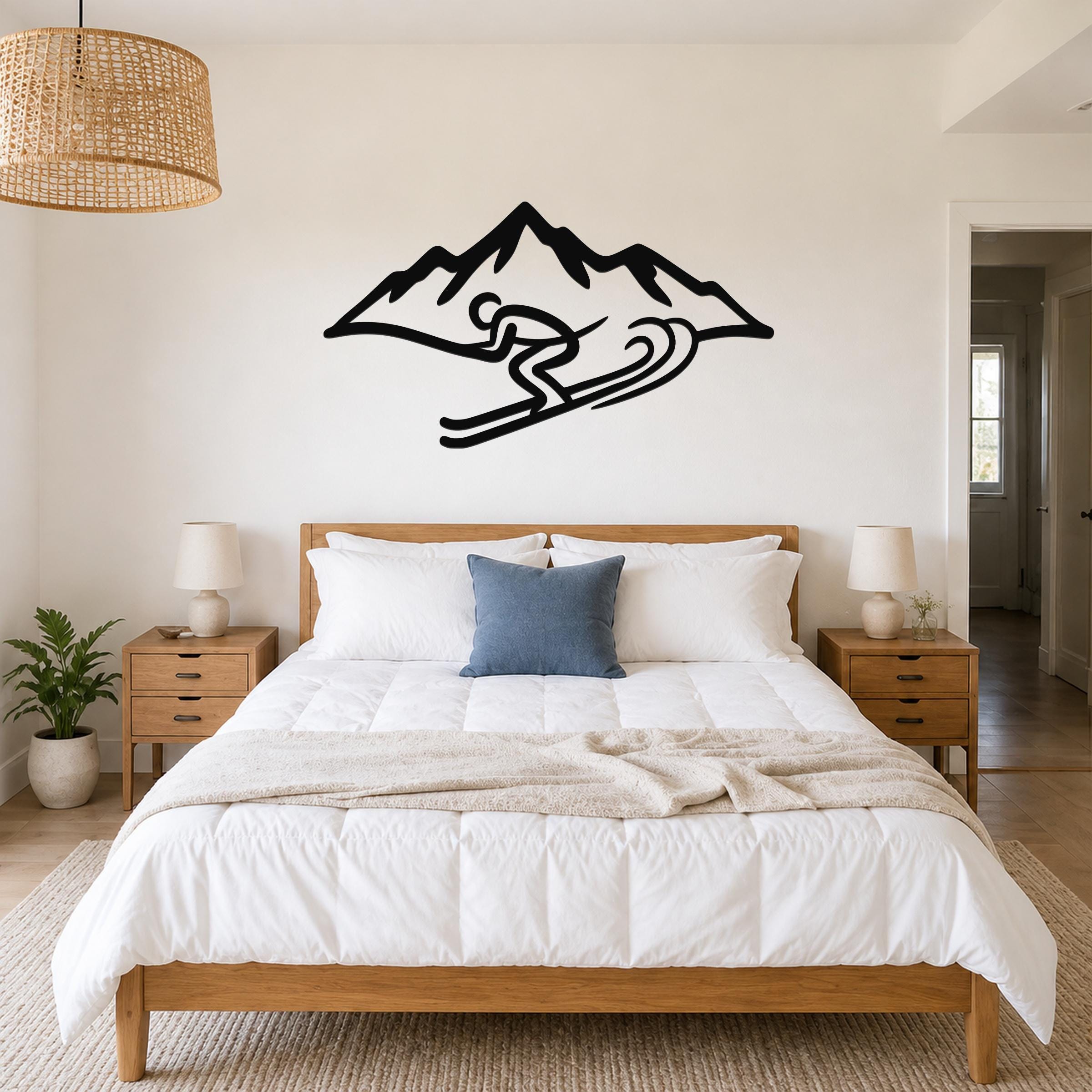 Black metal wall art featuring a skier silhouette in motion above a mountain peak, mounted on a bedroom wall above a wooden bed.
