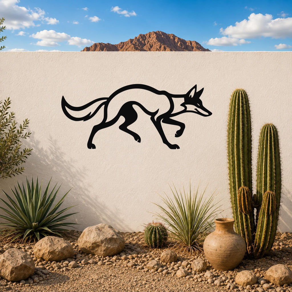 Black metal coyote wall art with a sleek silhouette, mounted on a white outdoor wall above a desert garden with cacti and rocks.